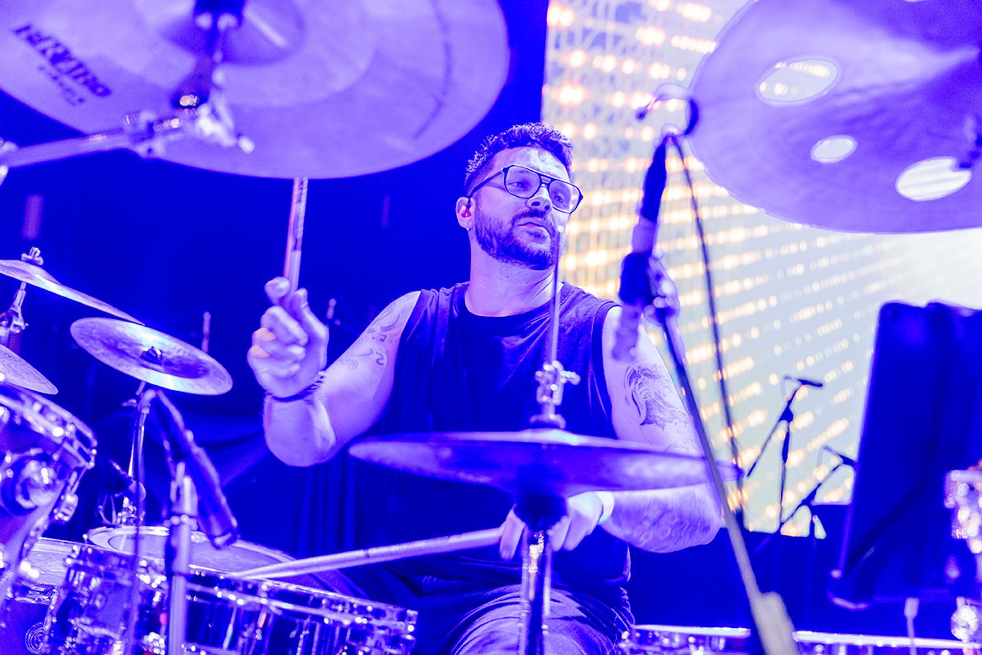 Um músico barbudo tocando bateria no palco sob uma intensa iluminação azul.