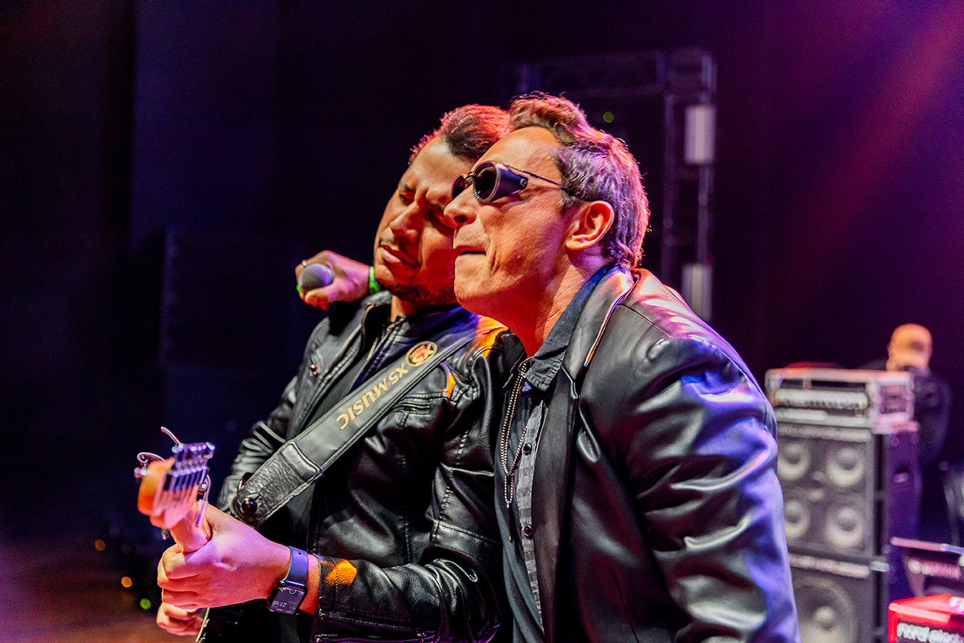 Dois músicos se apresentam no palco; um toca guitarra enquanto o outro canta