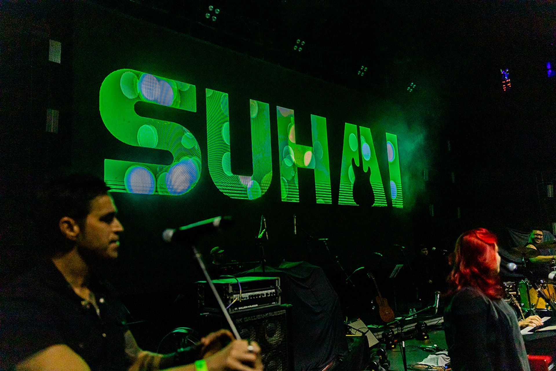 Vista do palco de uma banda sob um grande letreiro verde brilhante com a inscrição 