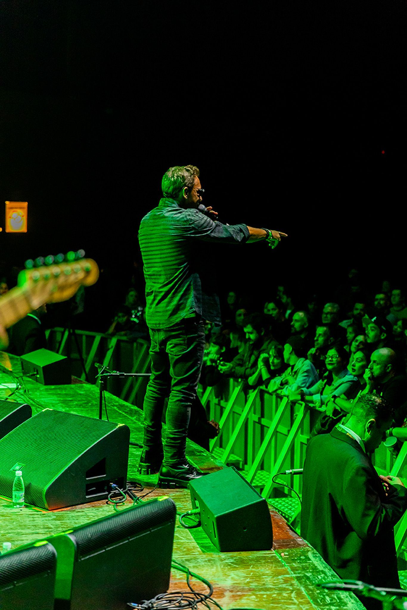 Um artista no palco apontando para a plateia em um show iluminado por luzes verdes.