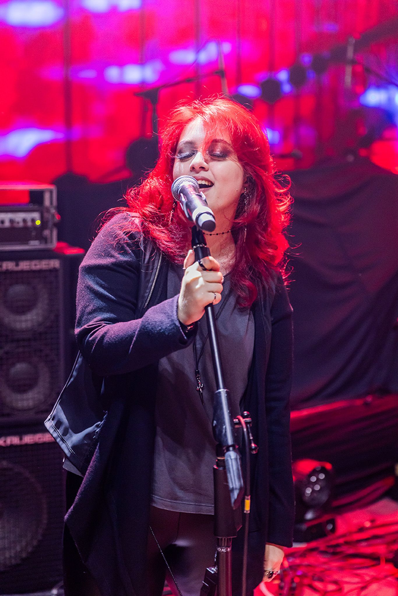 Um artista com cabelo vermelho vivo cantando em um microfone em um palco e equipamento de som.