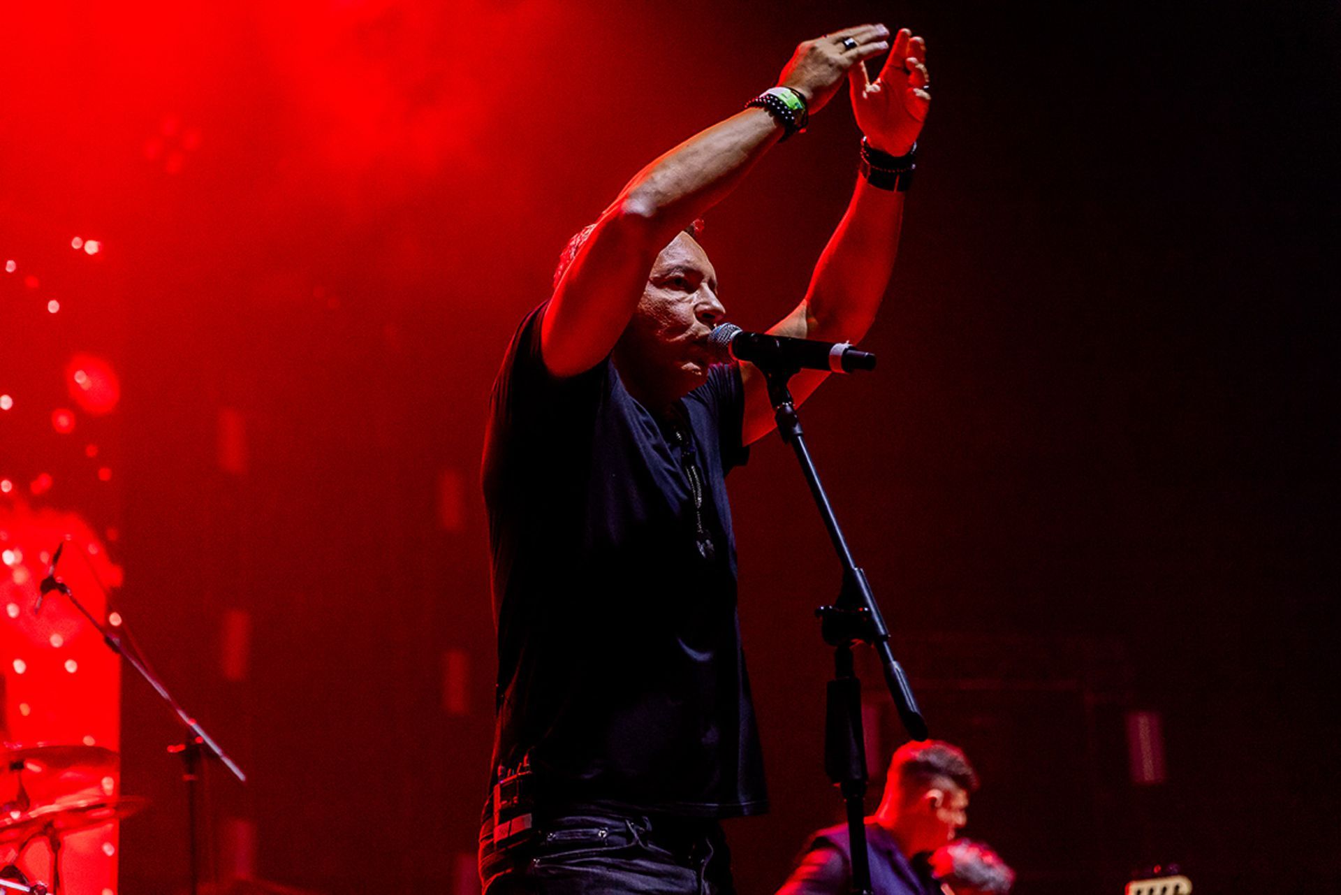 Um cantor se apresentando no palco sob luzes vermelhas, com os braços erguidos acima da cabeça .