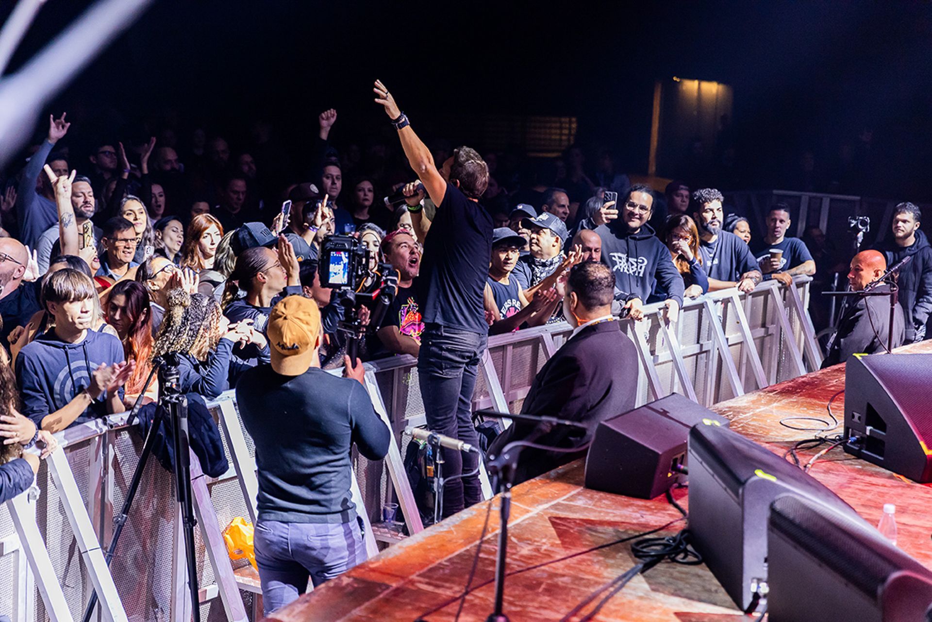 Um artista está no palco com os braços erguidos diante da plateia em um show, visto do palco em direção ao público.
