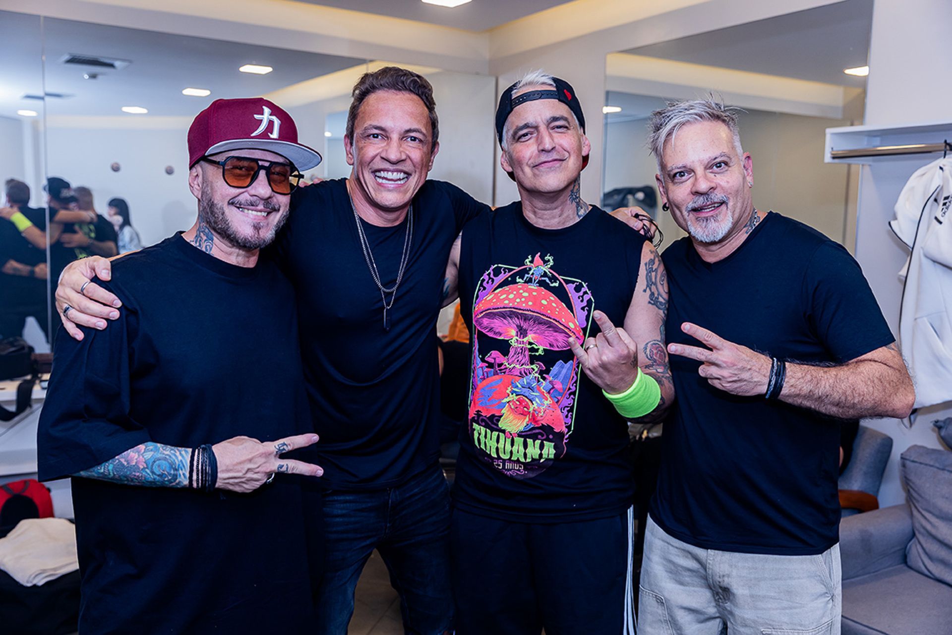 Quatro homens sorrindo e posando para uma foto de grupo em ambiente interno, alguns usando chapéus e roupas casuais.