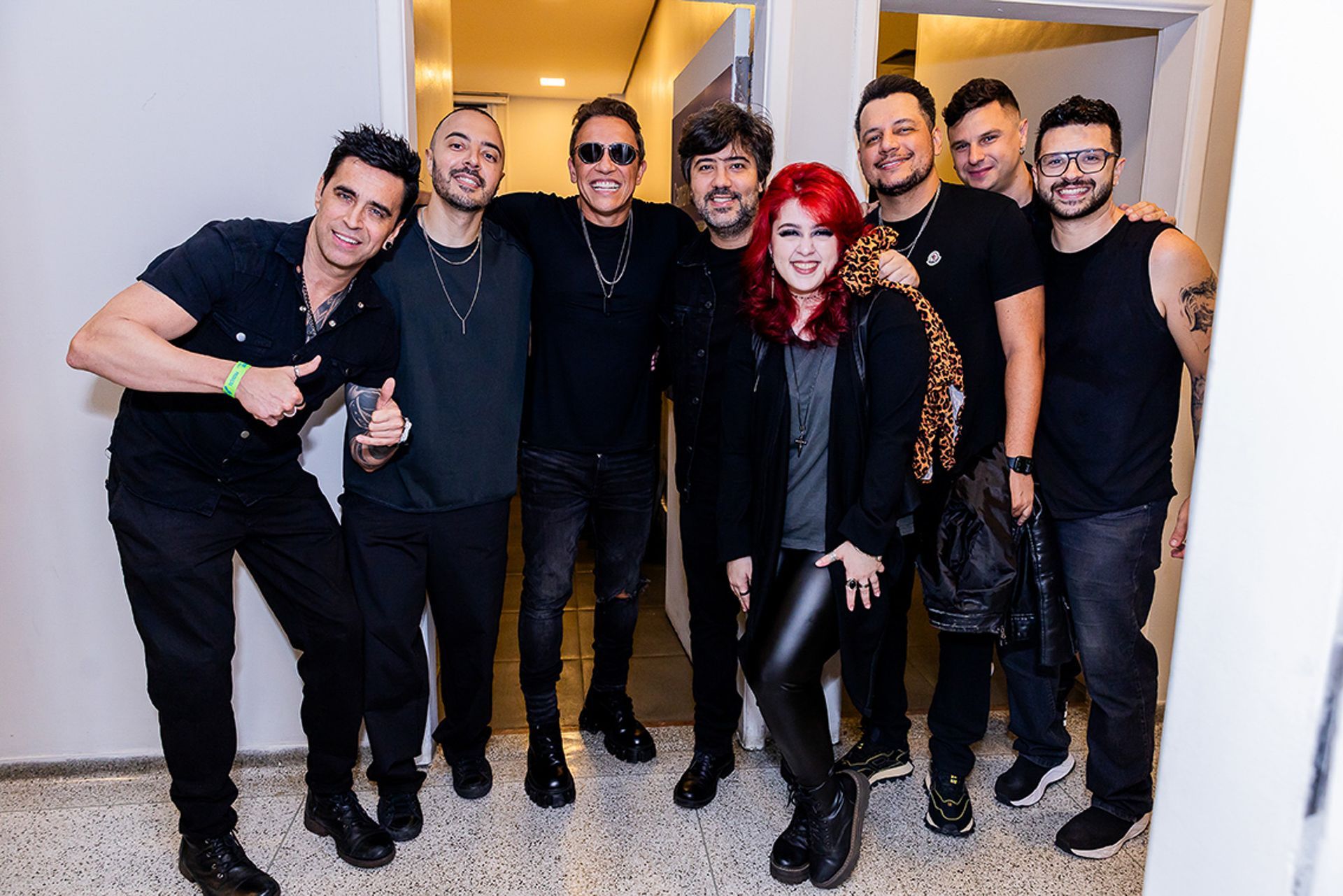 Um grupo de oito pessoas vestidas de preto, em pé juntas em um corredor interno bem iluminado.