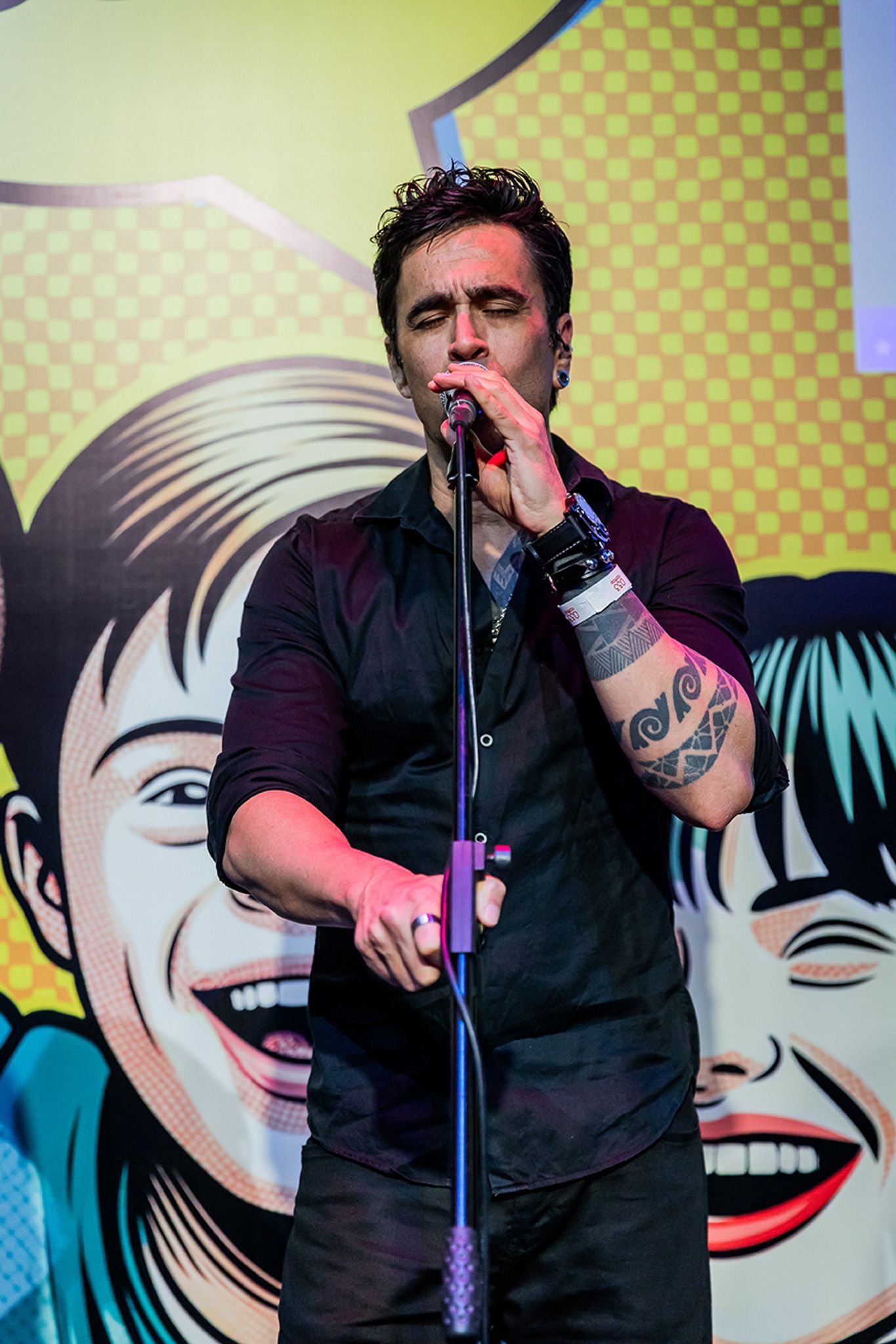 Um artista vestindo uma camisa preta se apresentando ao microfone, em pé contra um fundo com ilustrações de quadrinhos.