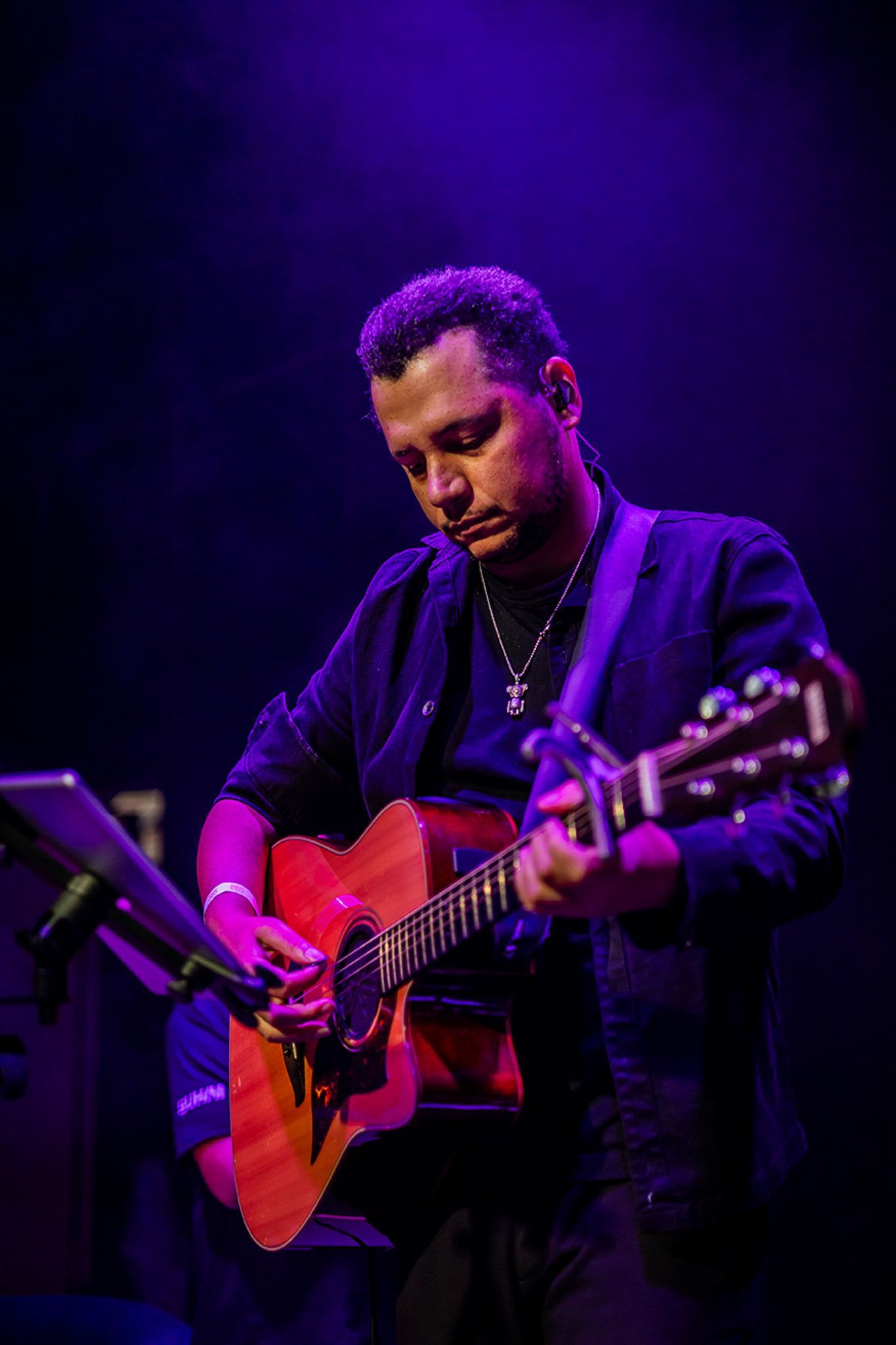Um músico, com foco no rosto, toca violão sob iluminação azul no palco.
