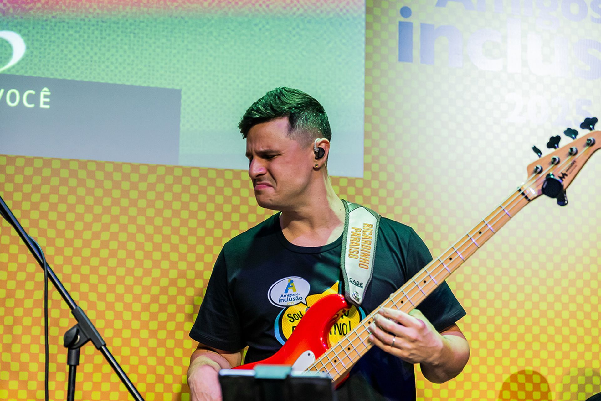 Um artista com expressão concentrada toca um baixo vermelho brilhante contra um fundo amarelo estampado.