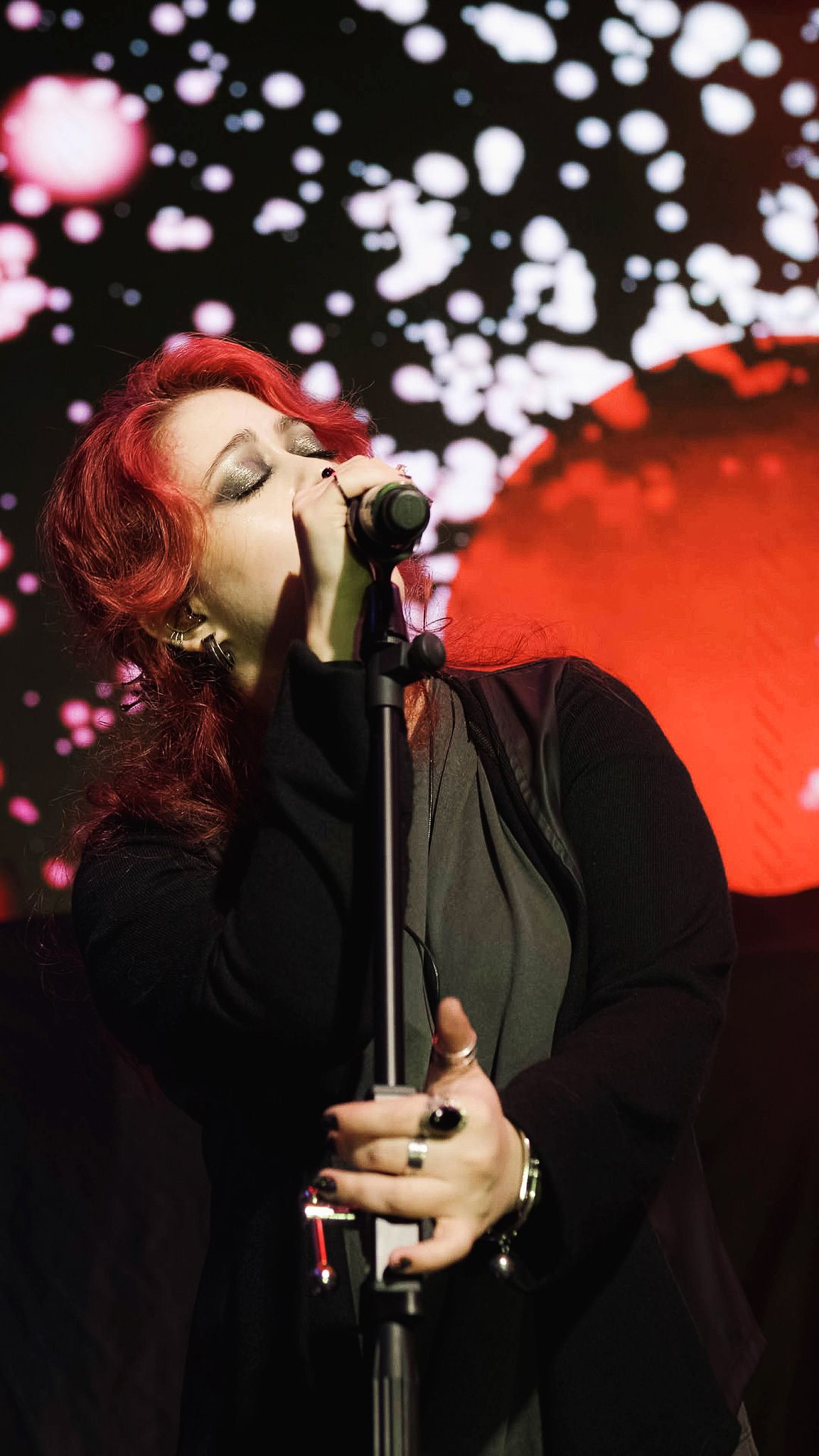 Uma pessoa com cabelos ruivos vibrantes cantando em um microfone no palco.