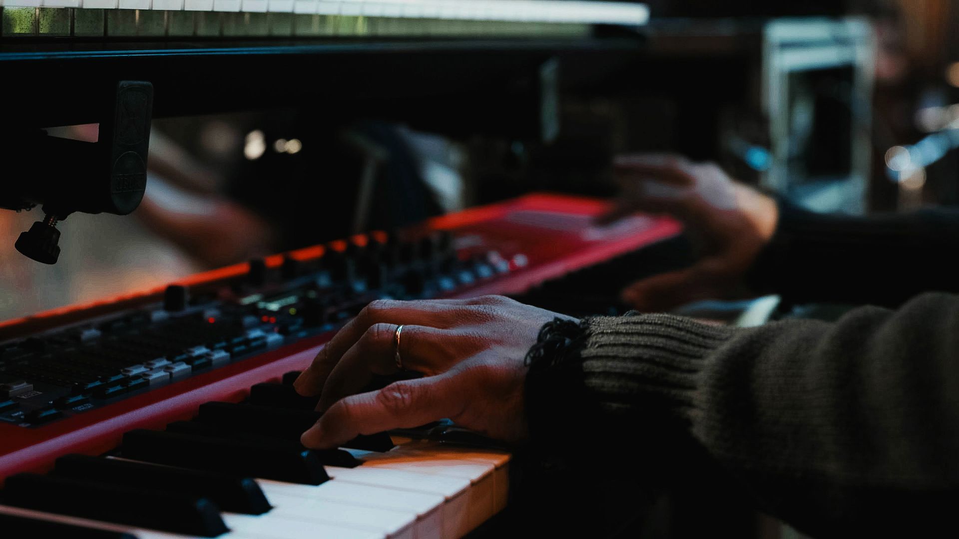 Mãos tocam um teclado vermelho em um ambiente com pouca luz.