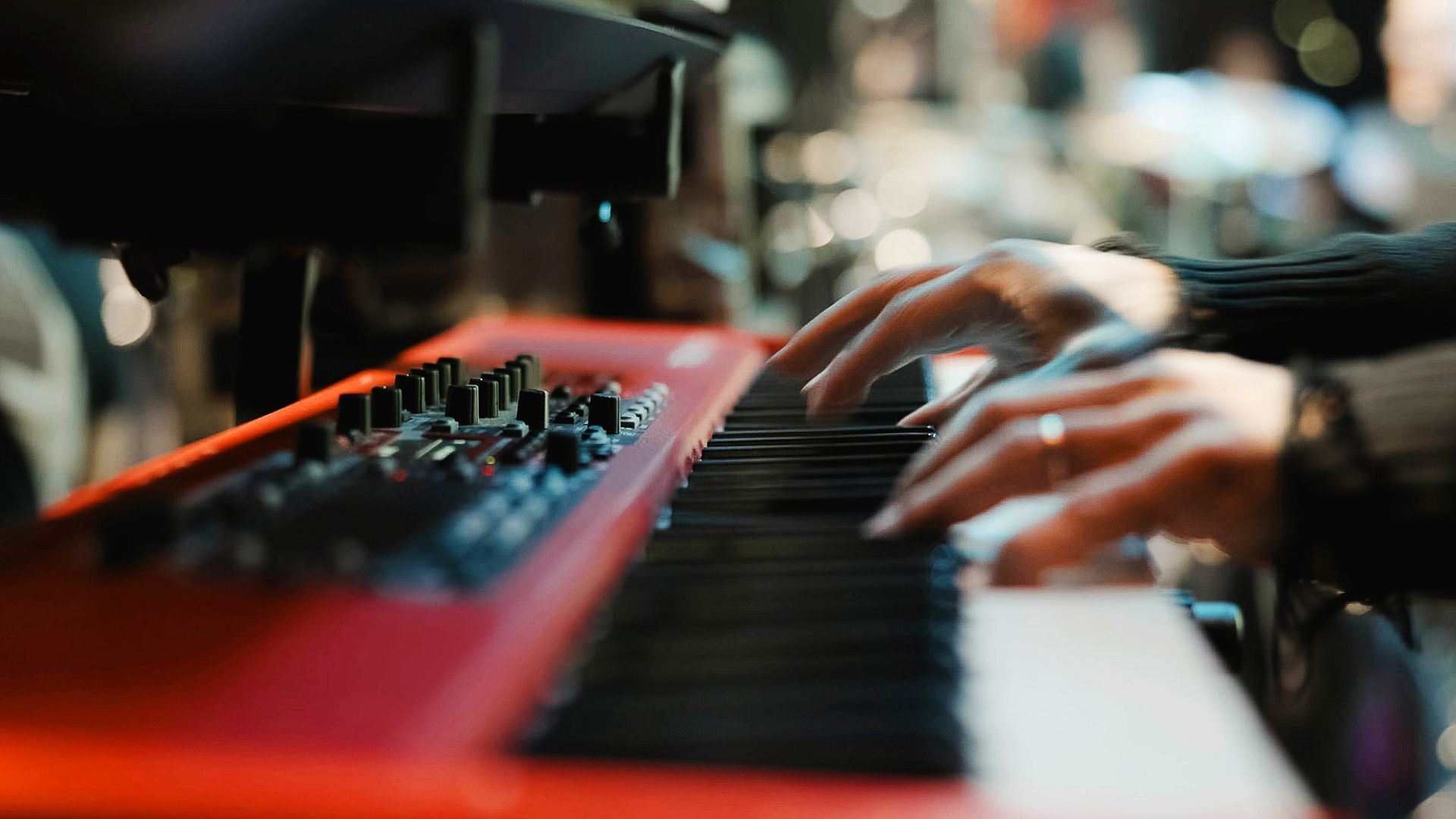 Mãos tocando um teclado de piano digital vermelho brilhante em um ambiente com pouca luz.