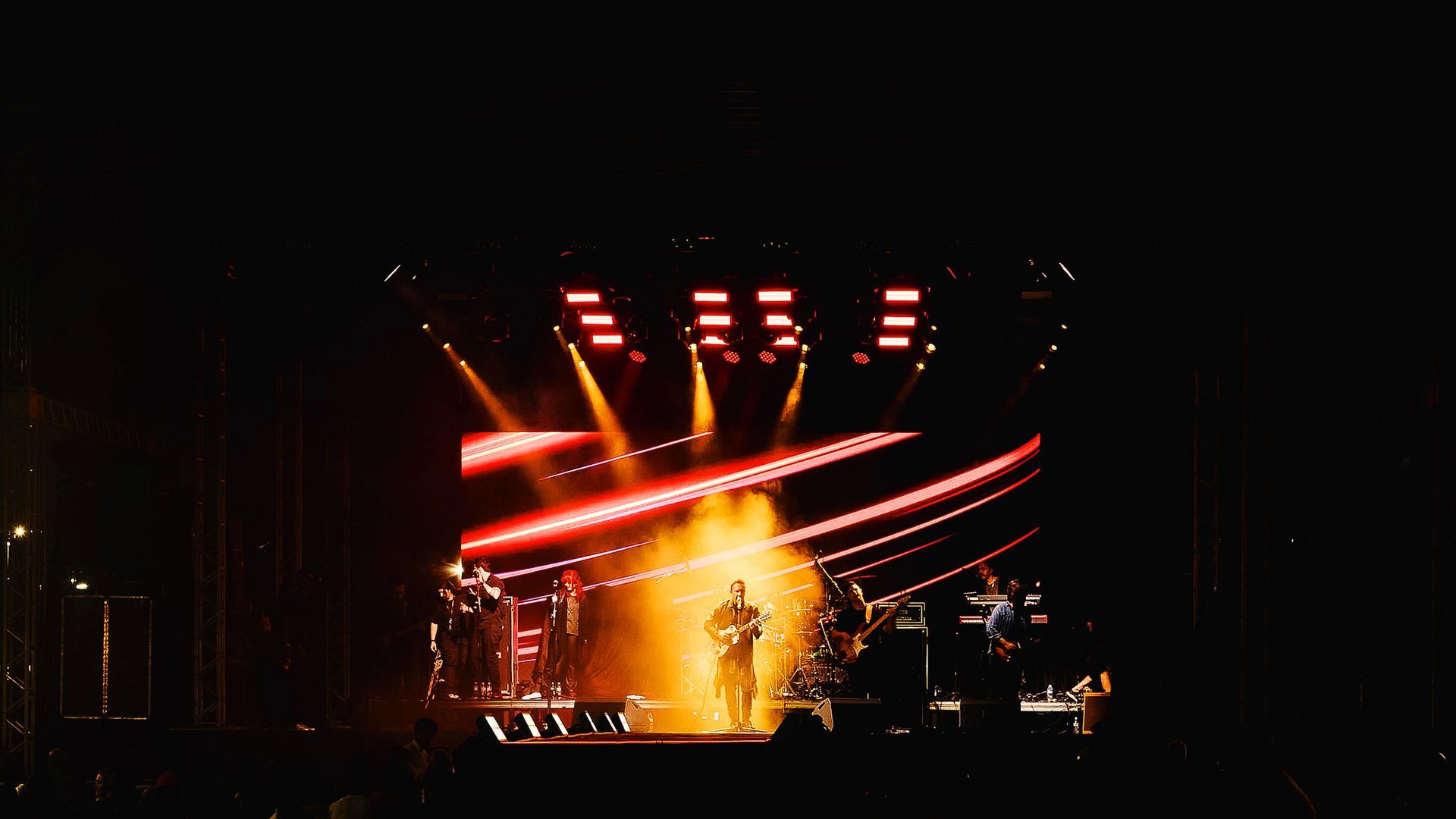 Um artista sob uma luz brilhante e quente em um palco escuro, emoldurado por iluminação cênica vermelha e efeitos de fumaça.