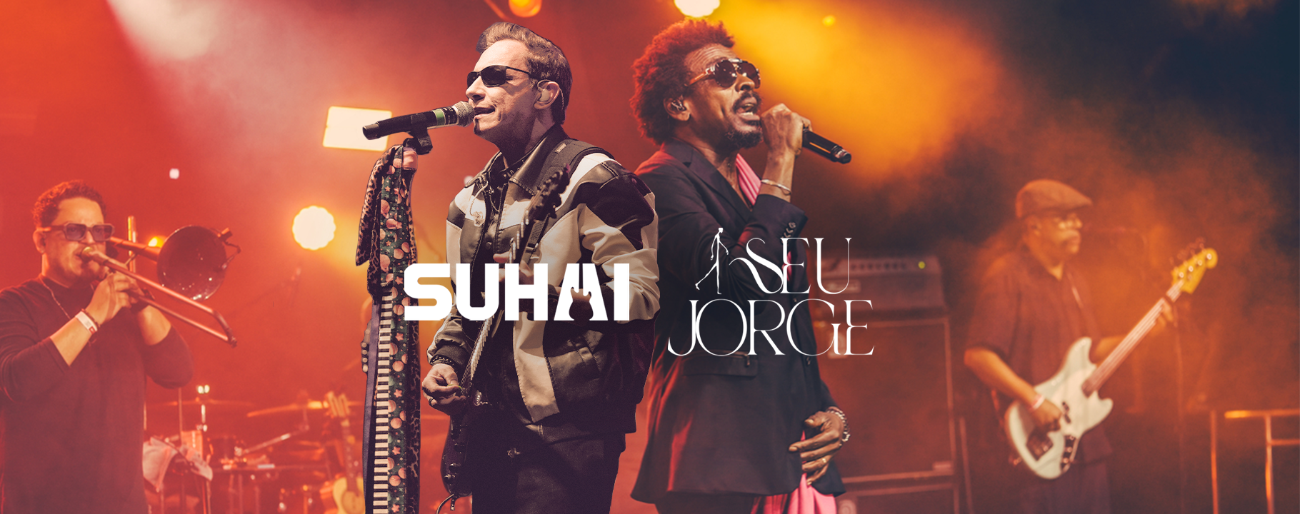 Banda se apresentando no palco com cantores e músicos, iluminados por luzes de palco laranja.