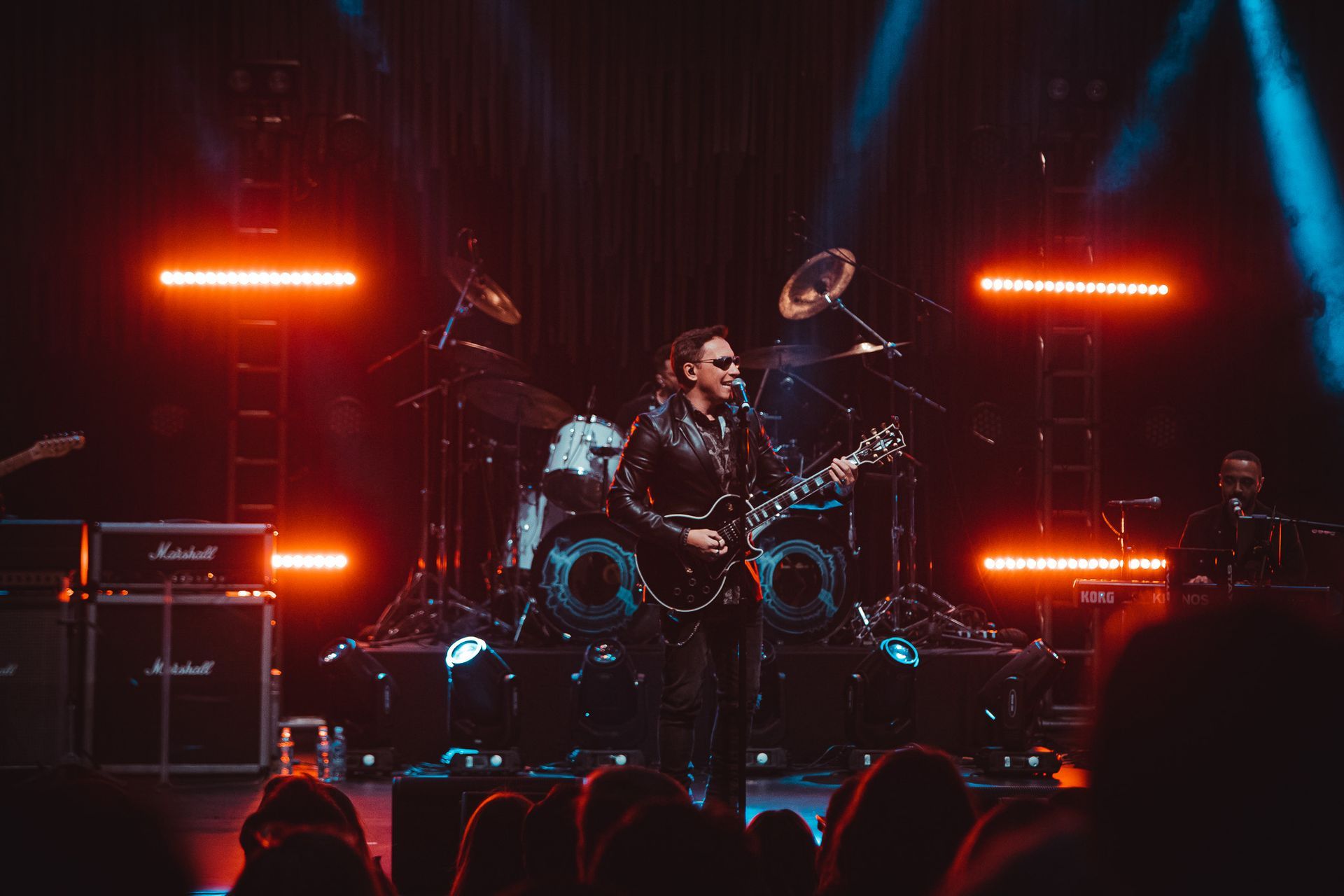Um músico tocando guitarra elétrica em um palco escuro iluminado por luzes de palco horizontais laranja brilhantes.