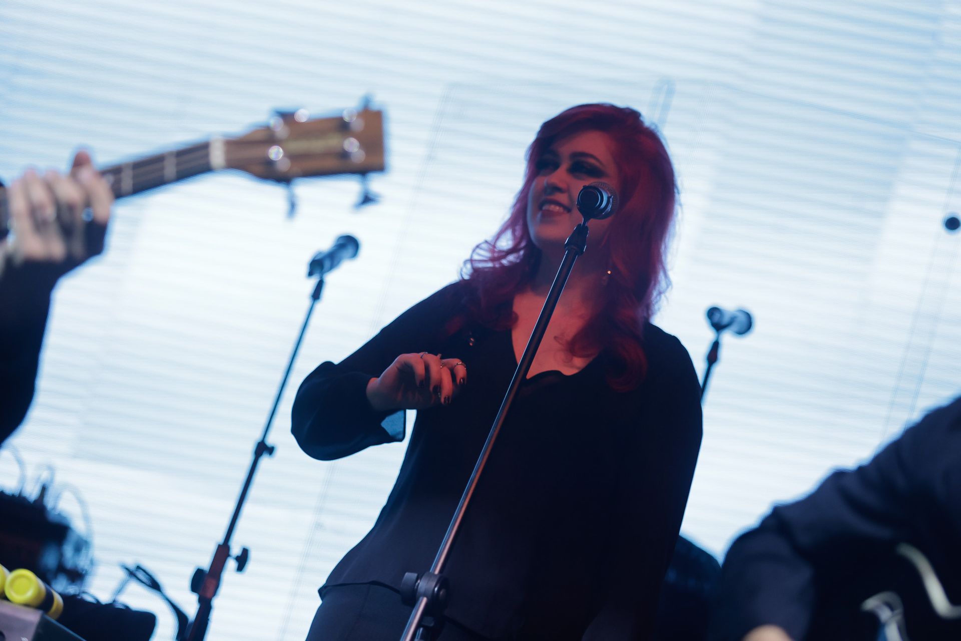Uma artista ruiva cantando ao microfone no palco; banda ao fundo.