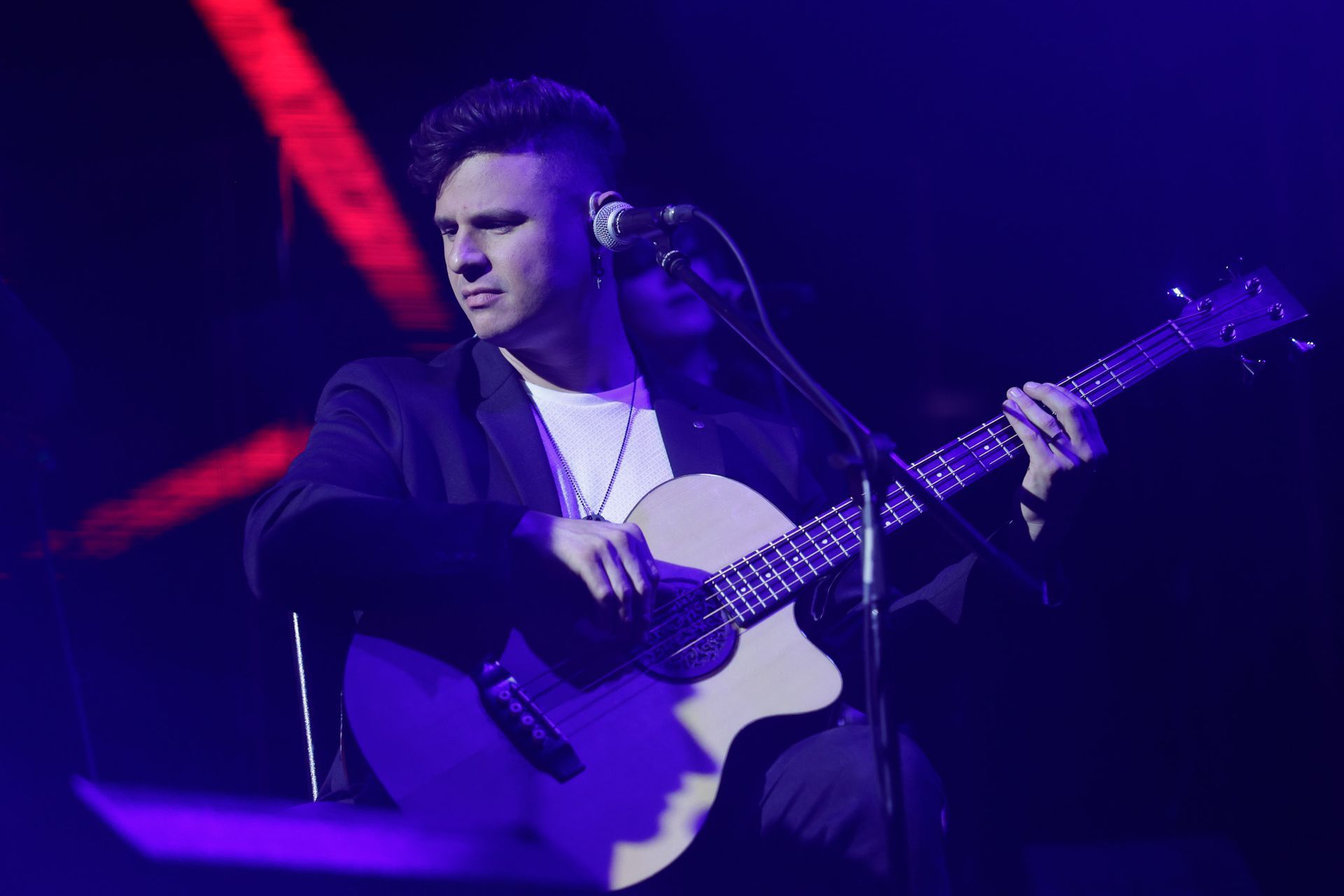Um artista tocando baixo no palco, iluminado com luzes azuis e vermelhas.