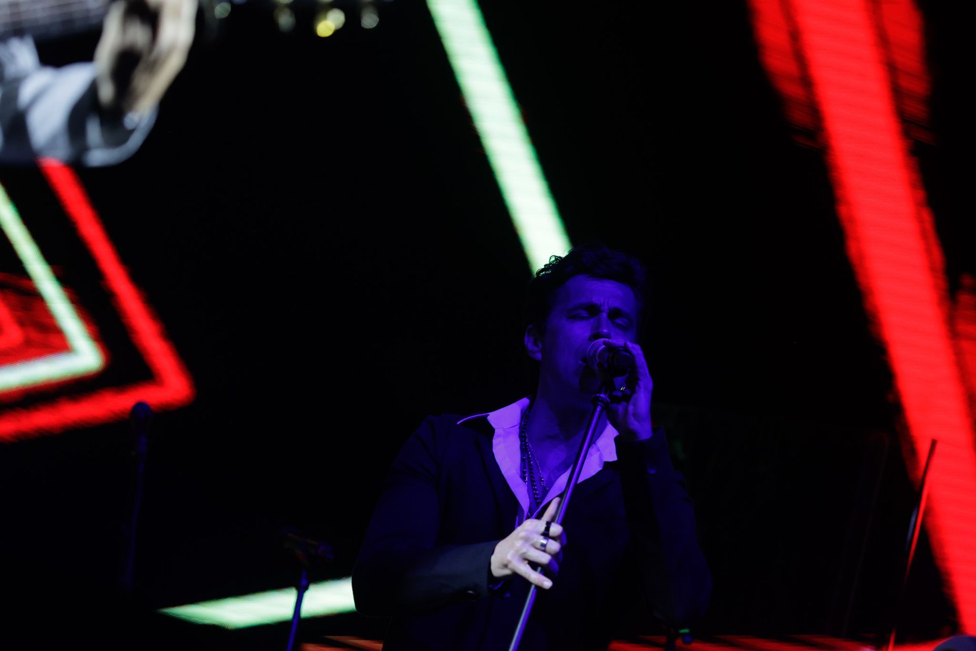 Um artista cantando em um microfone no palco, sob luzes coloridas.