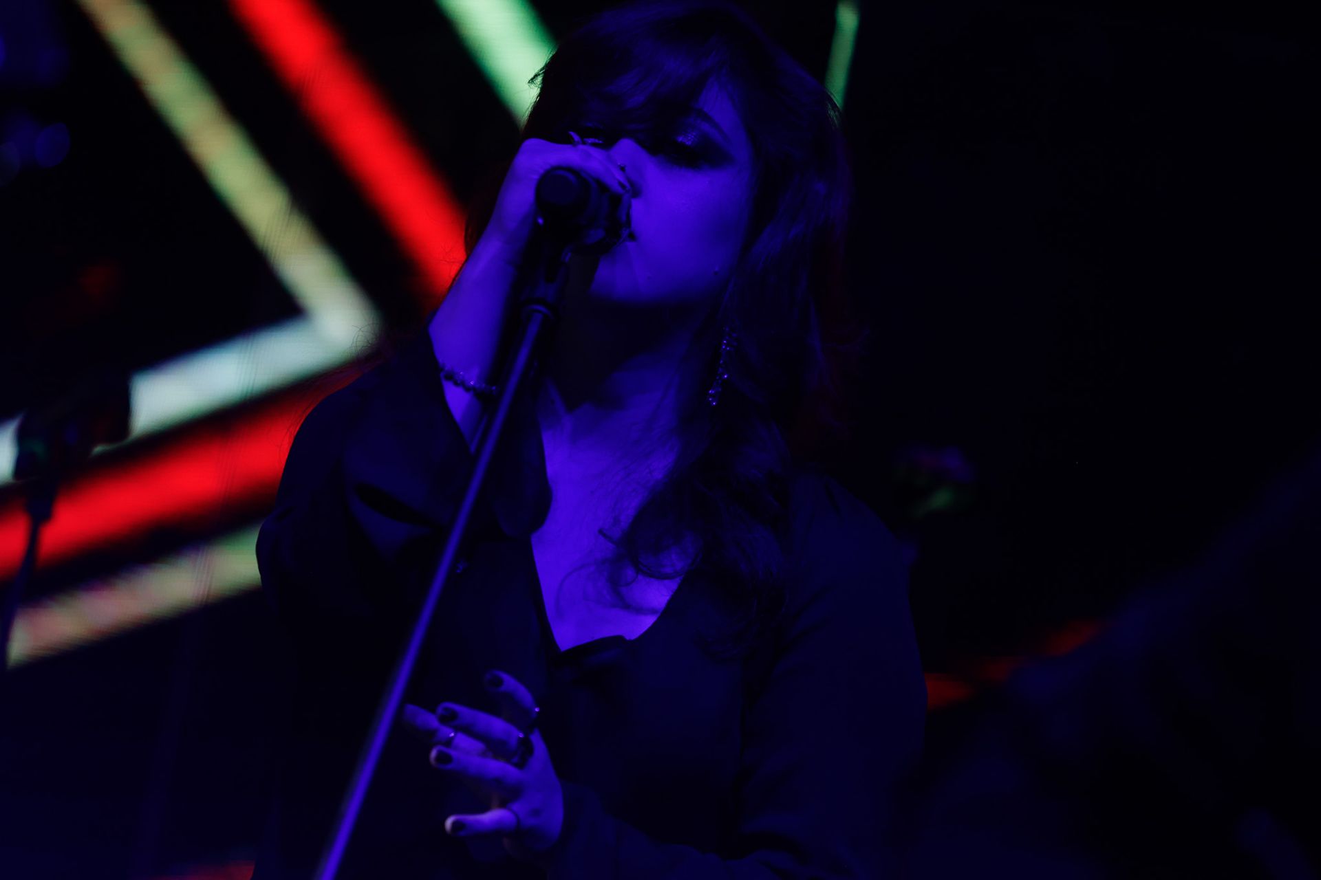 Uma artista cantando em um microfone no palco, iluminado com luzes azuis e de néon.