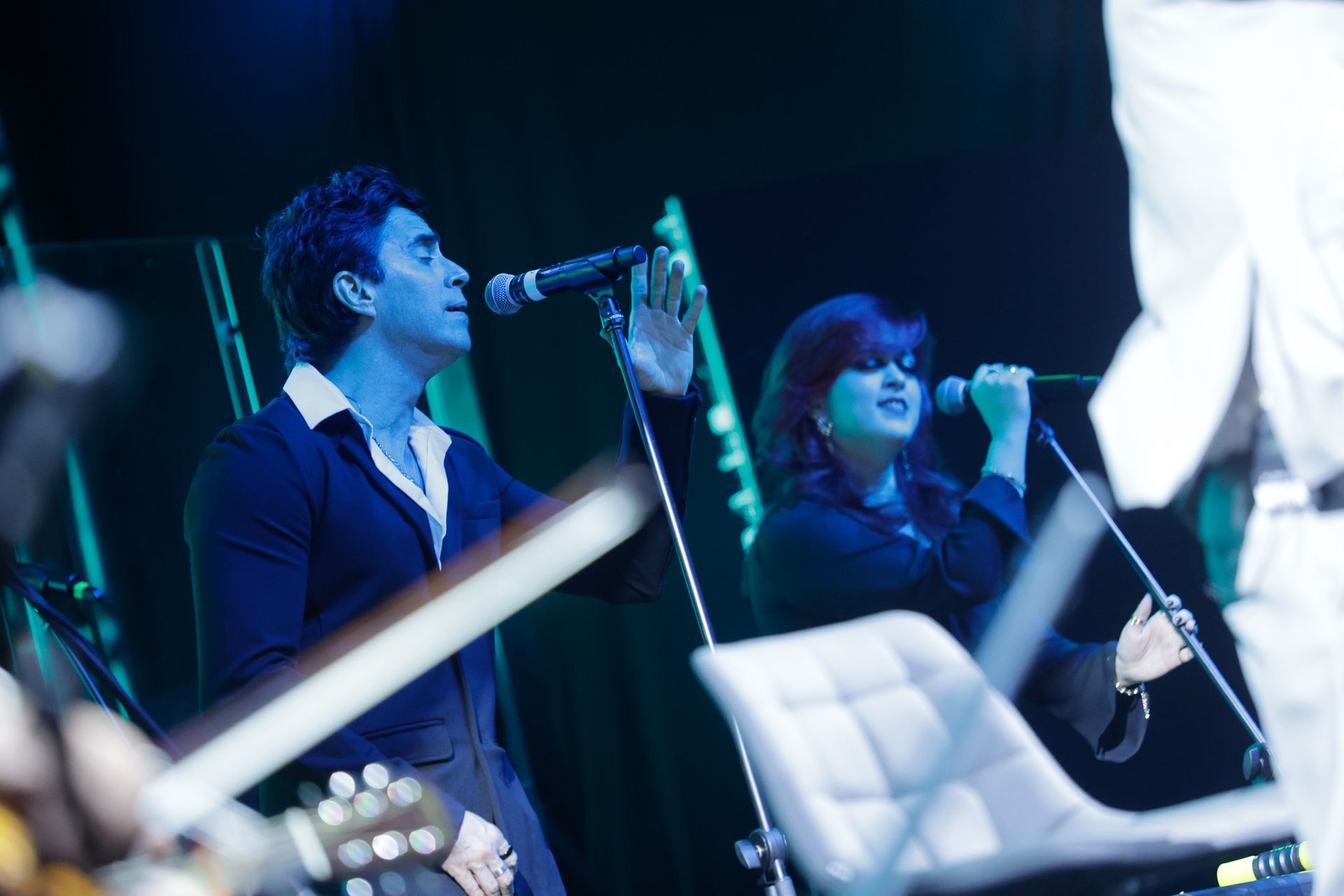 Cantores se apresentam no palco, iluminadas por luz azul. 