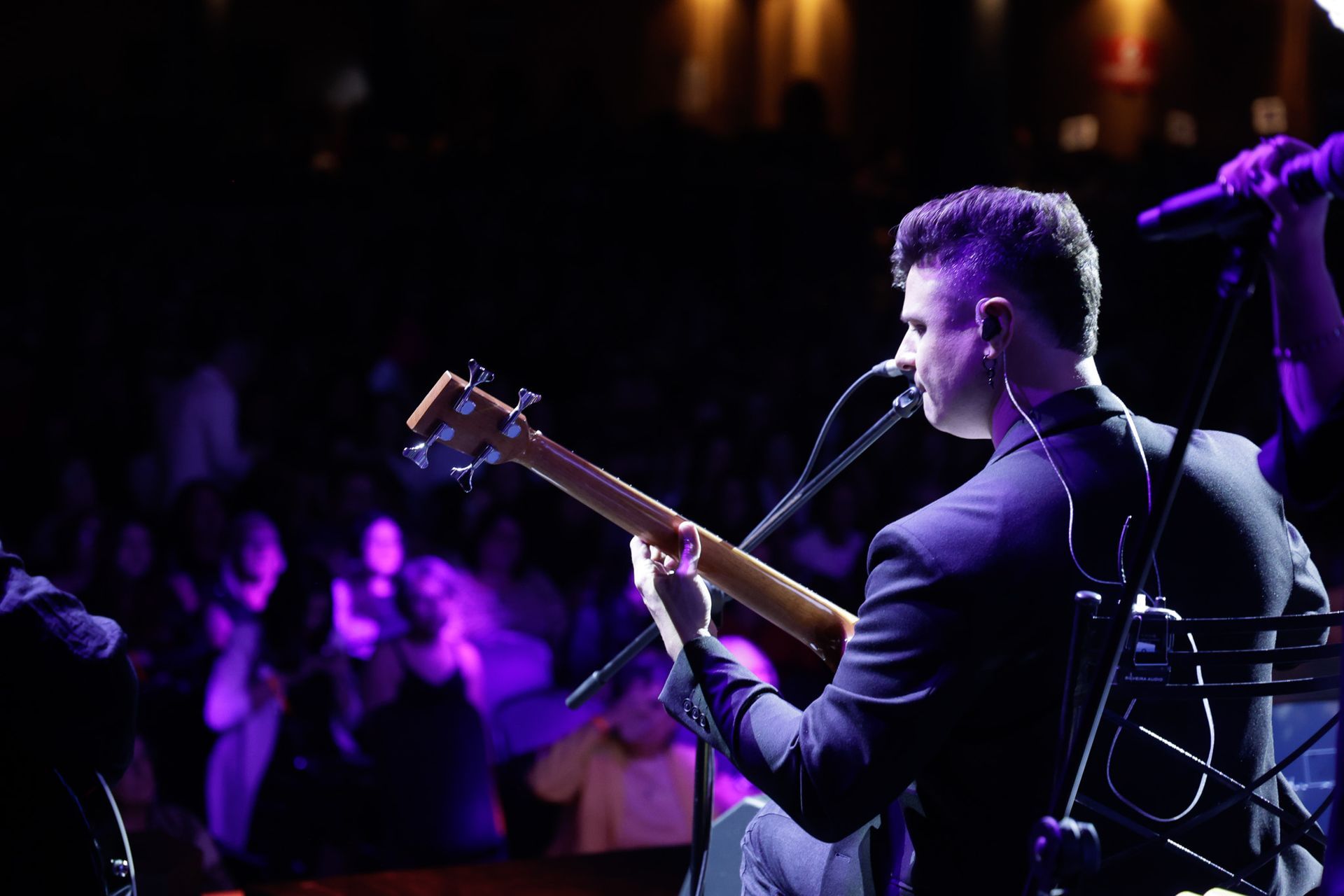 Um artista tocando baixo no palco com iluminação roxa.