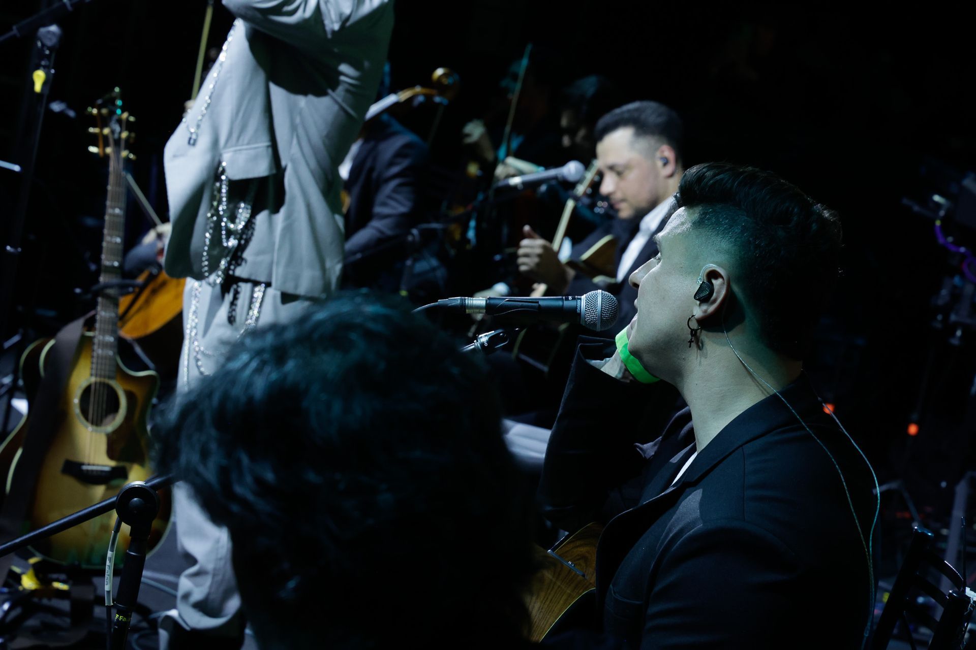 Cantor se apresentando no palco com uma banda, incluindo um violinista.