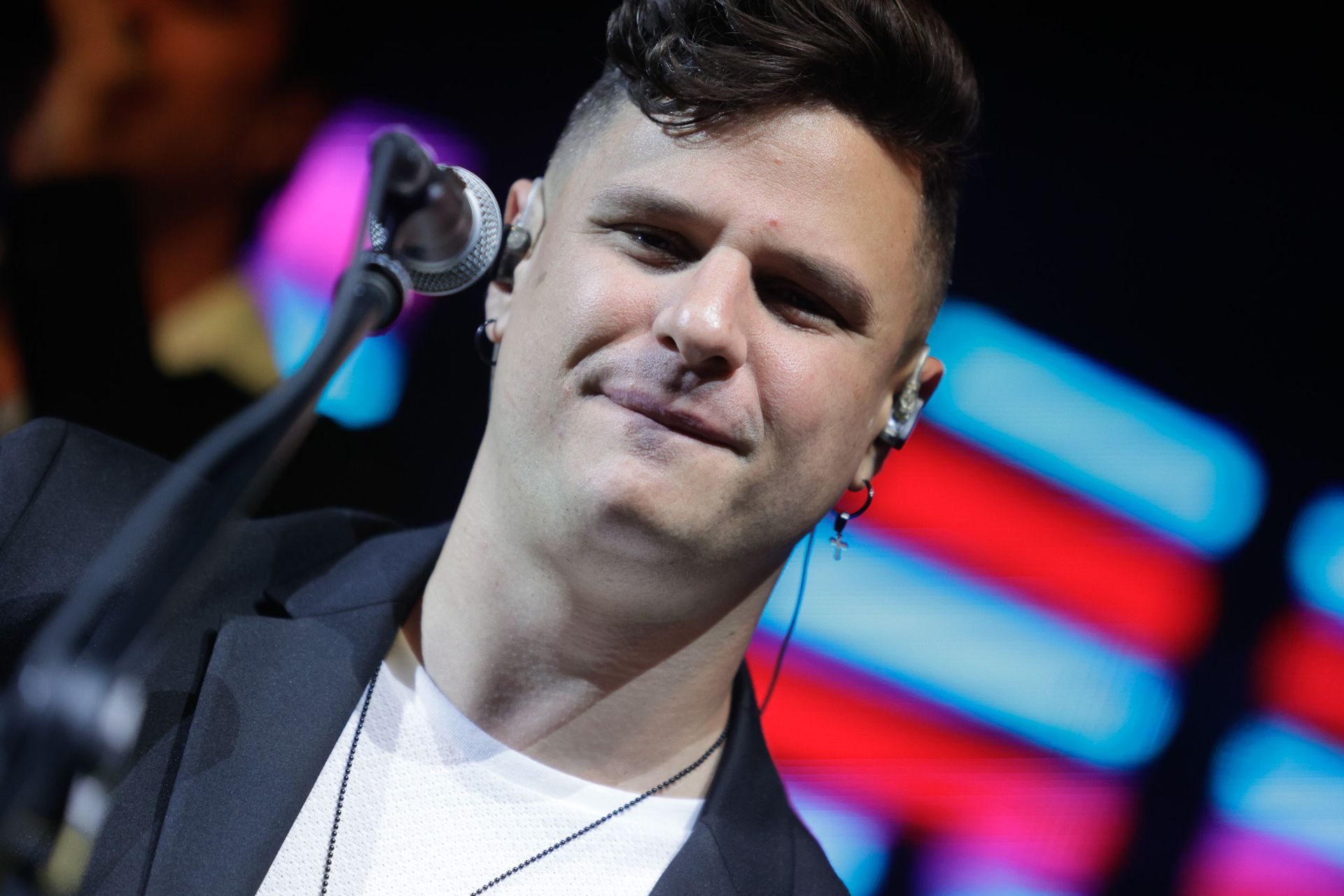 Um artista de cabelos escuros e terno, cantando ao microfone no palco.