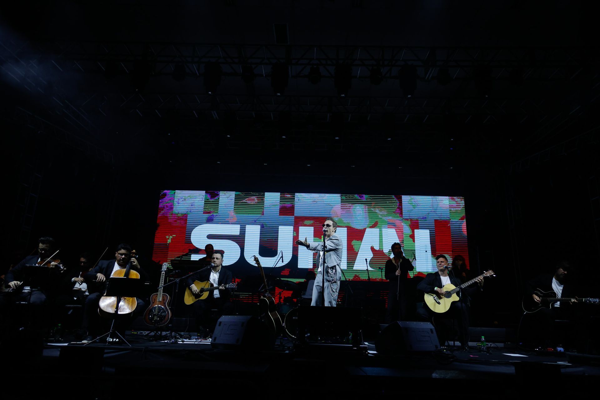Banda se apresentando no palco em frente a uma tela exibindo 