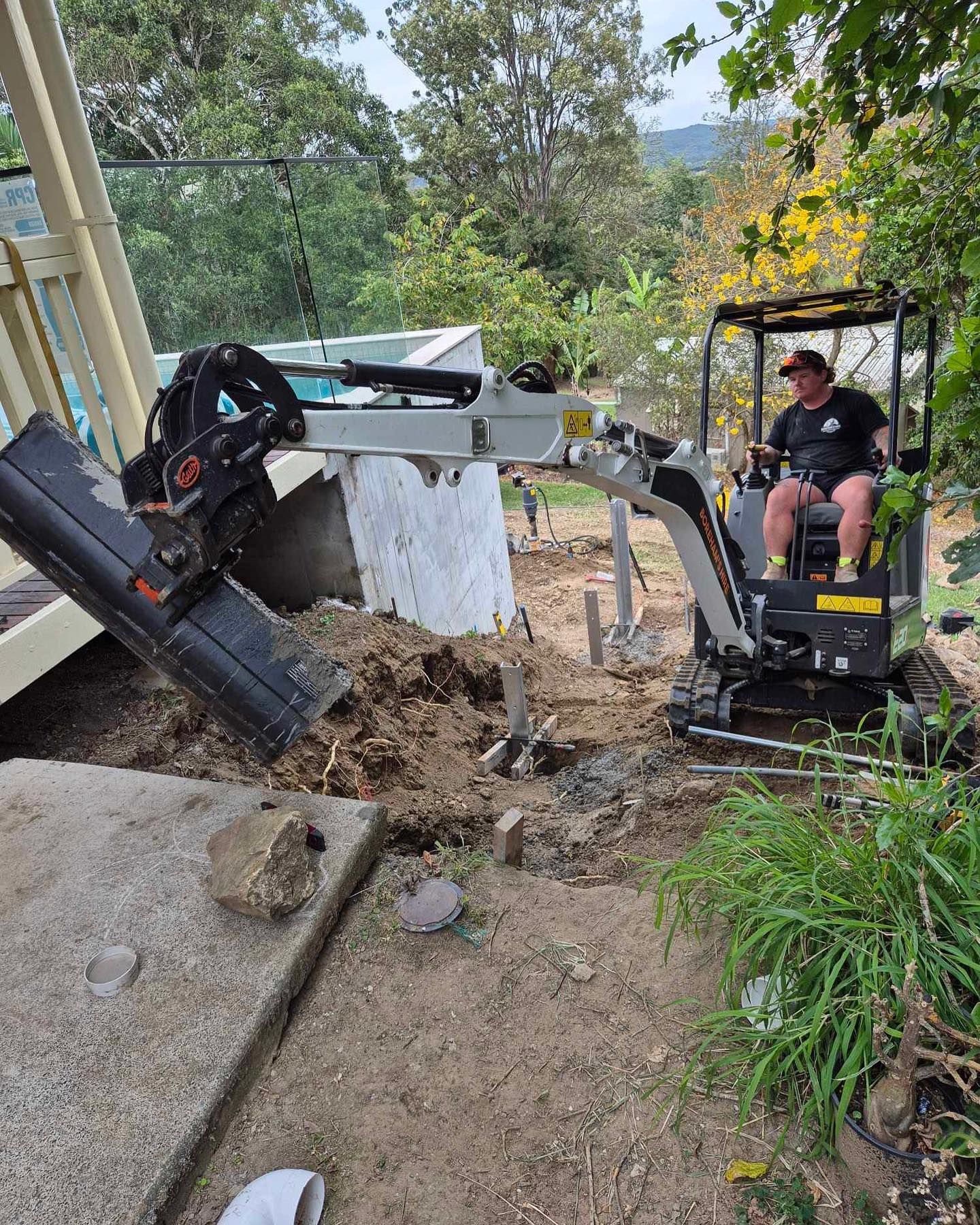 Person Operating a Small Excavator, Digging Near a Concrete Structure — Borehams Hire In Meridan Plains, QLD