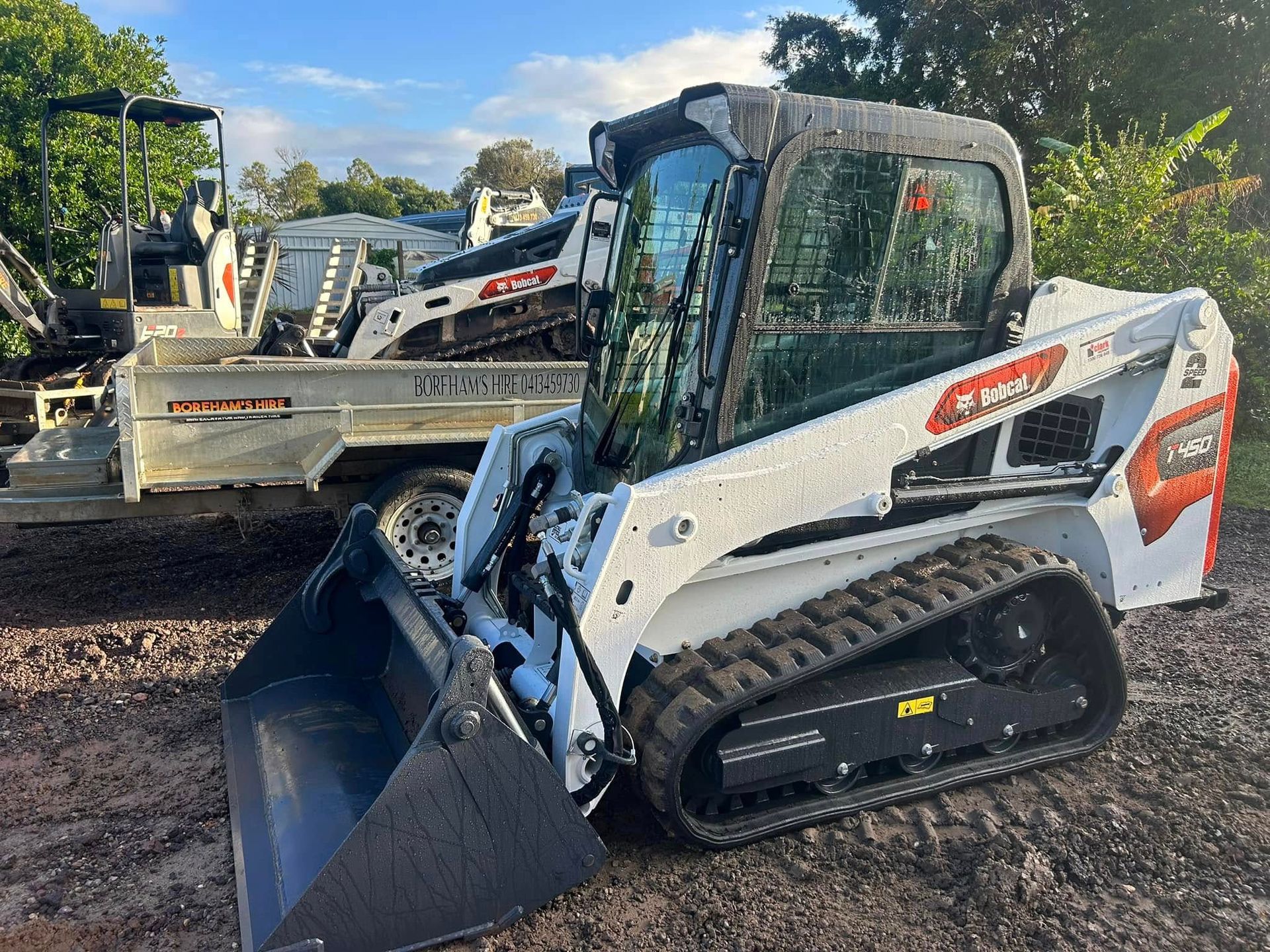 White Bobcat Track Loader Parked, Bucket Down, Near Other Machinery — Borehams Hire In Meridan Plains, QLD