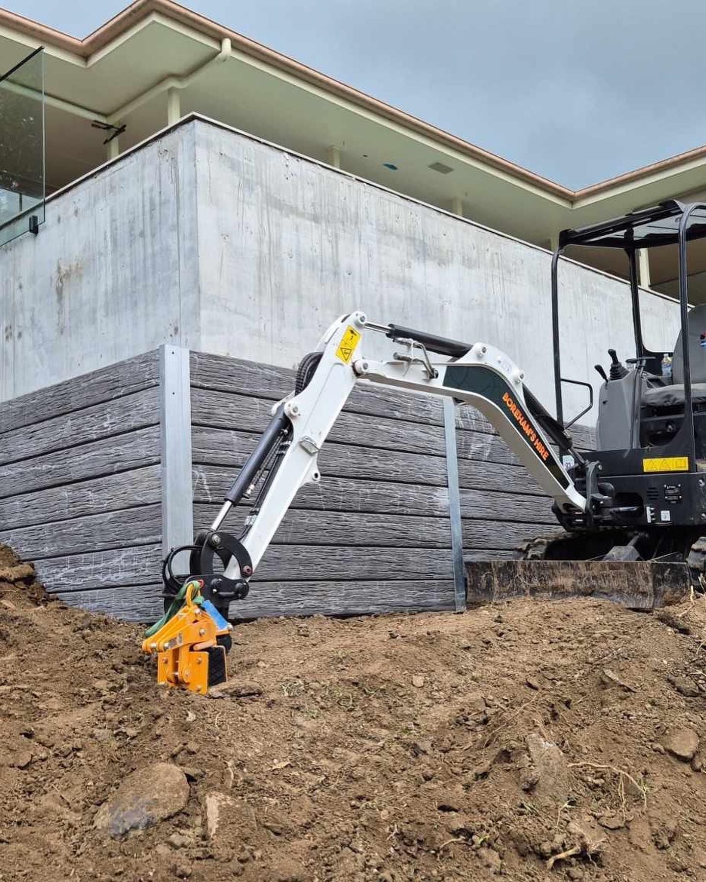 Mini Excavator Compacting Soil Near a Retaining Wall — Borehams Hire In Meridan Plains, QLD