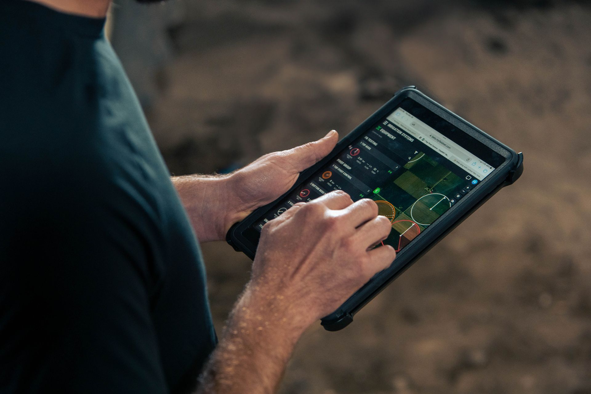 A person uses a rugged tablet to view aerial mapping data of agricultural fields while standing outdoors.
