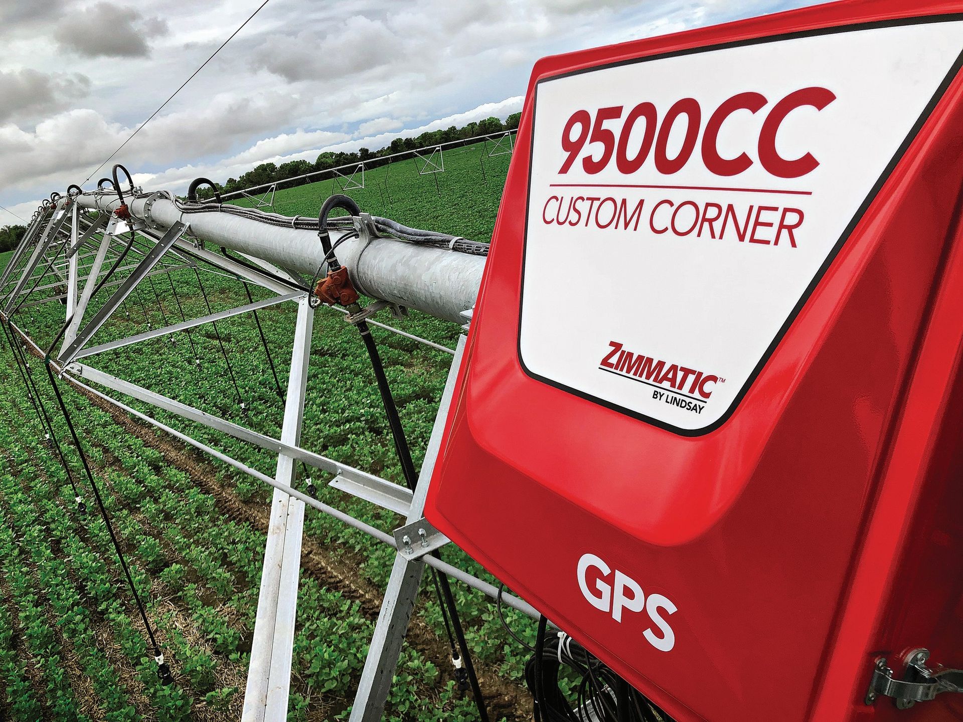 A close-up of a red Zimmatic 9500CC GPS-controlled irrigation corner arm in a green field under a cloudy sky.