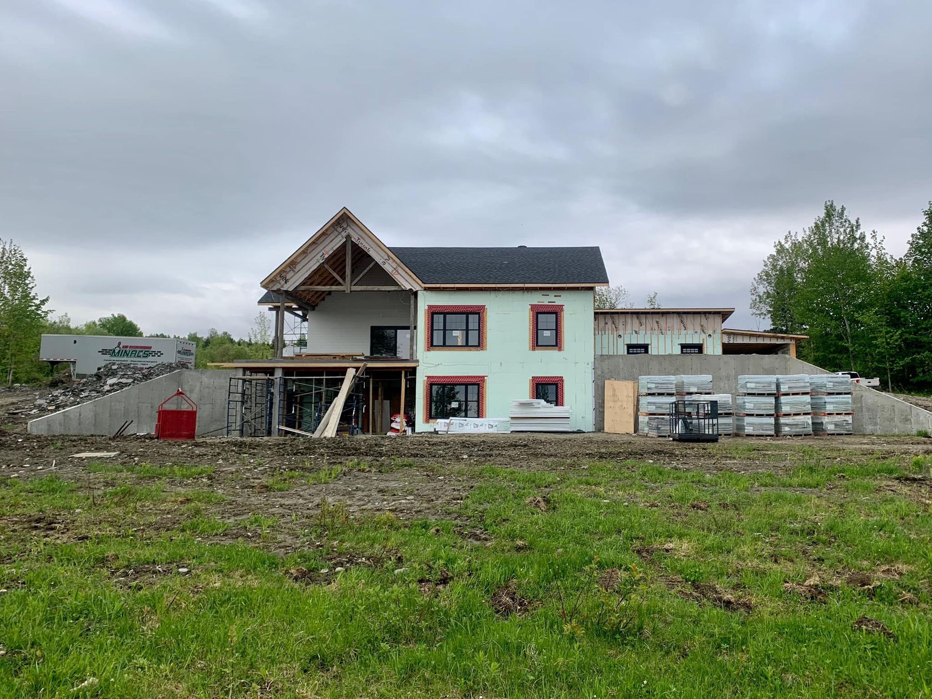 Maison en construction avec revêtement vert, garniture rouge et poutres de toit apparentes.
