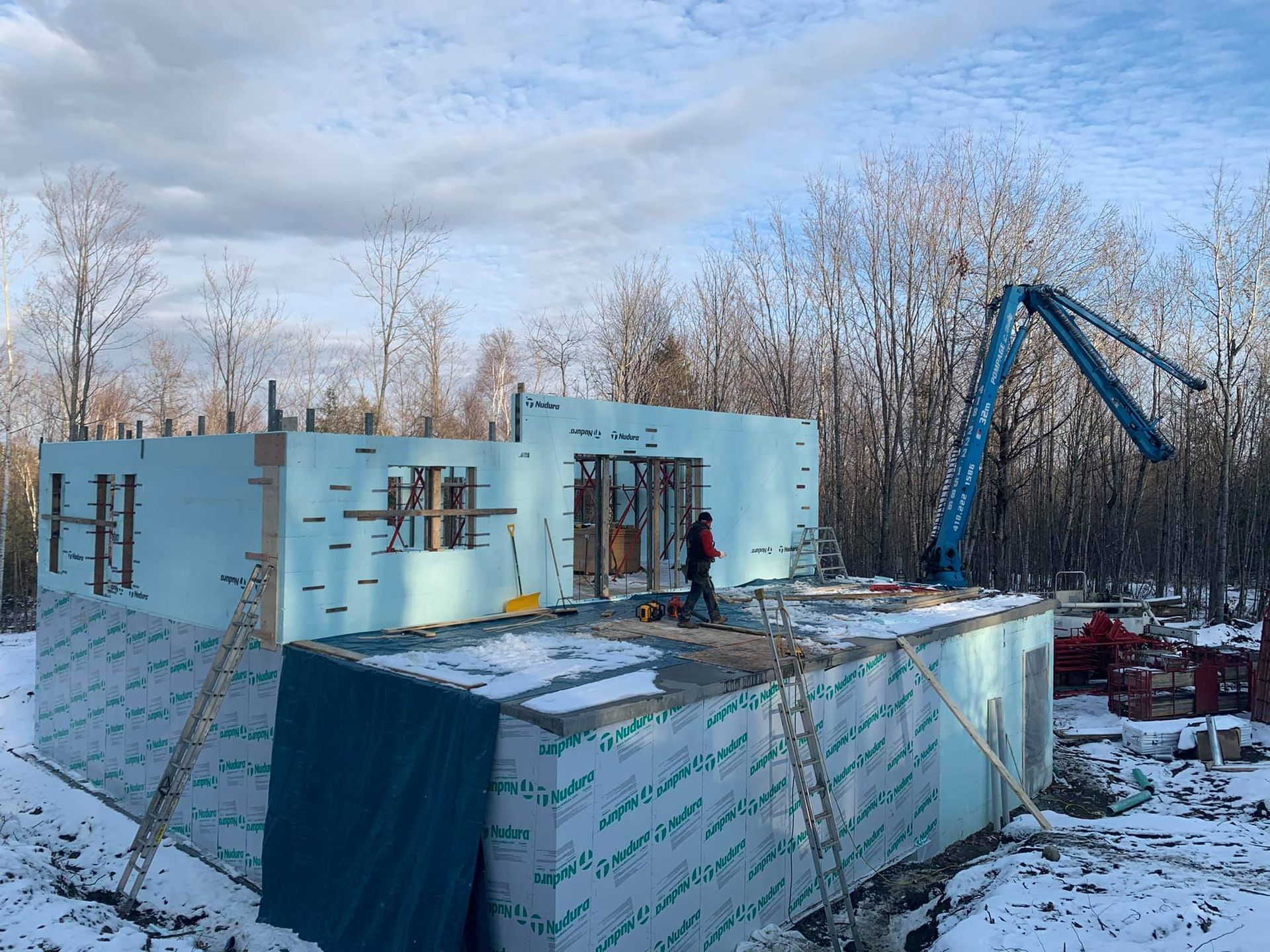 Construction d'un bâtiment avec des panneaux isolants bleus, de la neige et une pompe à béton.