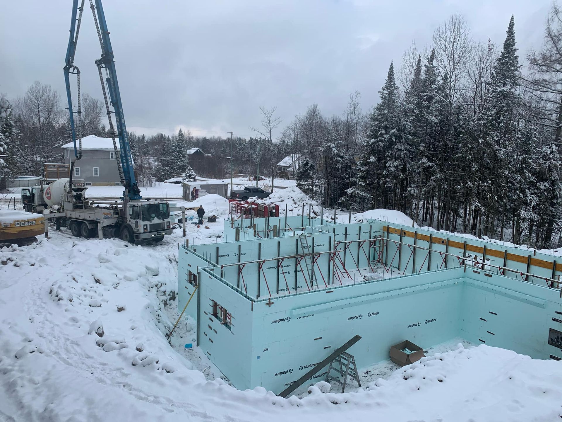 Chantier en hiver : Fondation en coffrage isolant, pompe à béton, terrain enneigé.