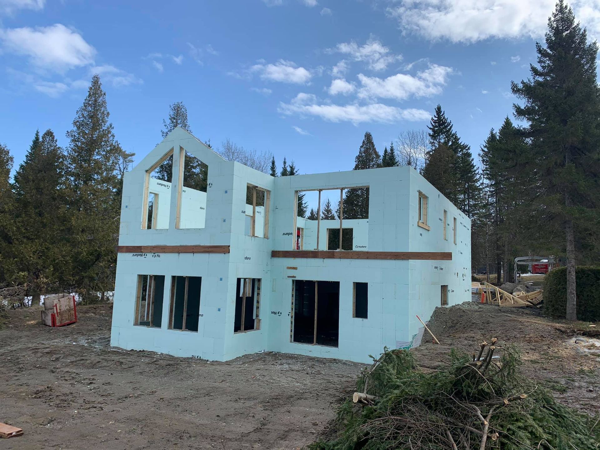 Maison à deux étages en construction; murs en béton isolé bleu, fenêtres encadrées, arrière-plan forestier.