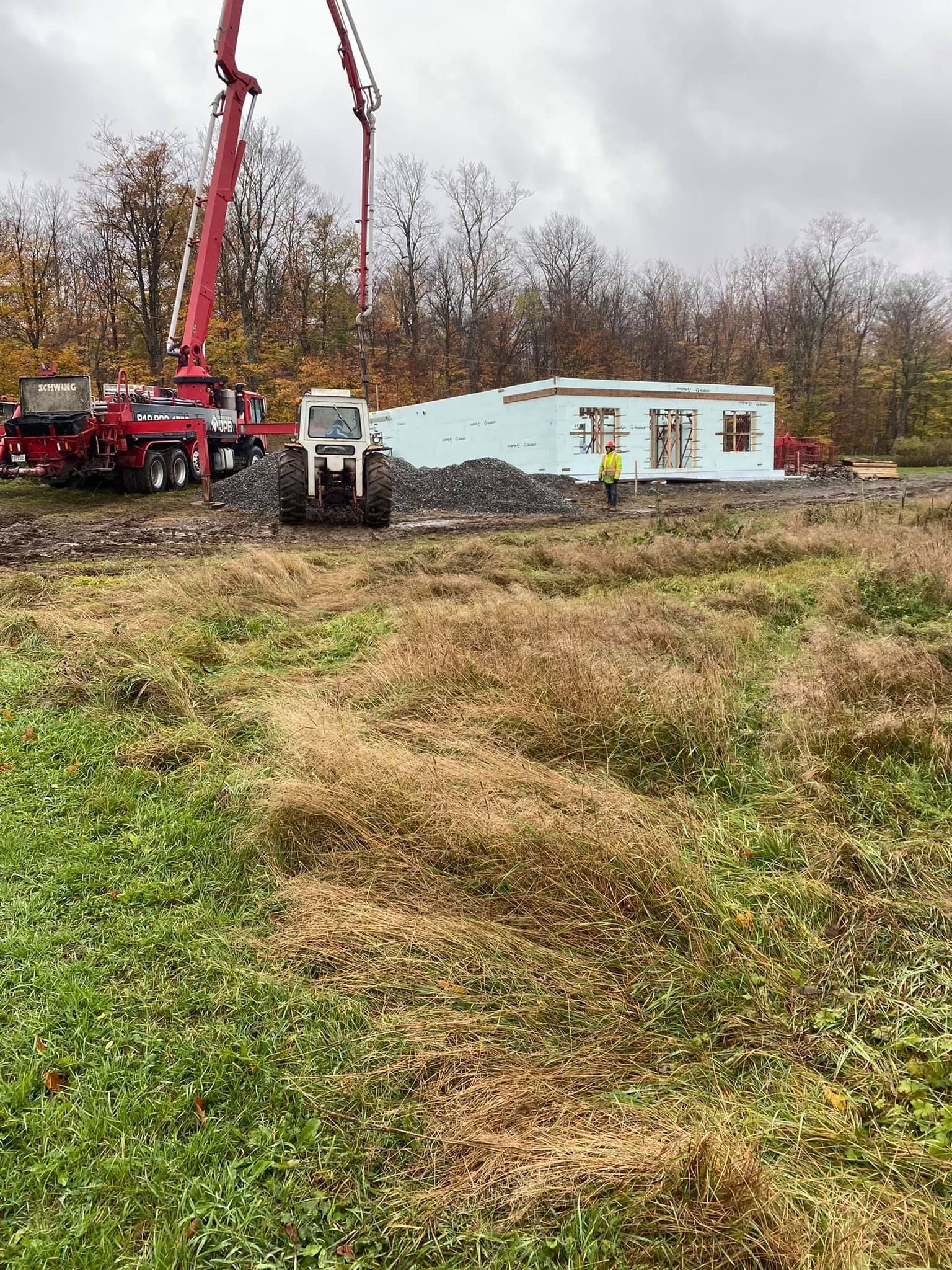 Chantier : camion pompe à béton, tracteur, maison partiellement construite, terrain vert et brun.