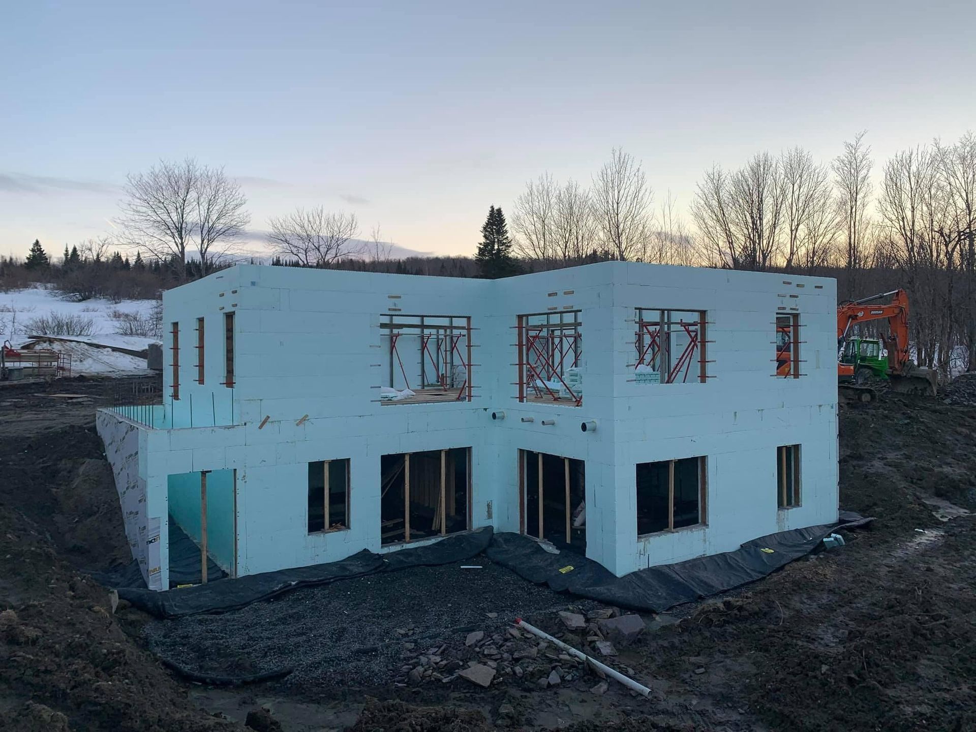 Maison à deux étages en construction. Murs en mousse bleu clair, fenêtres à encadrement en bois, terre et arbres.