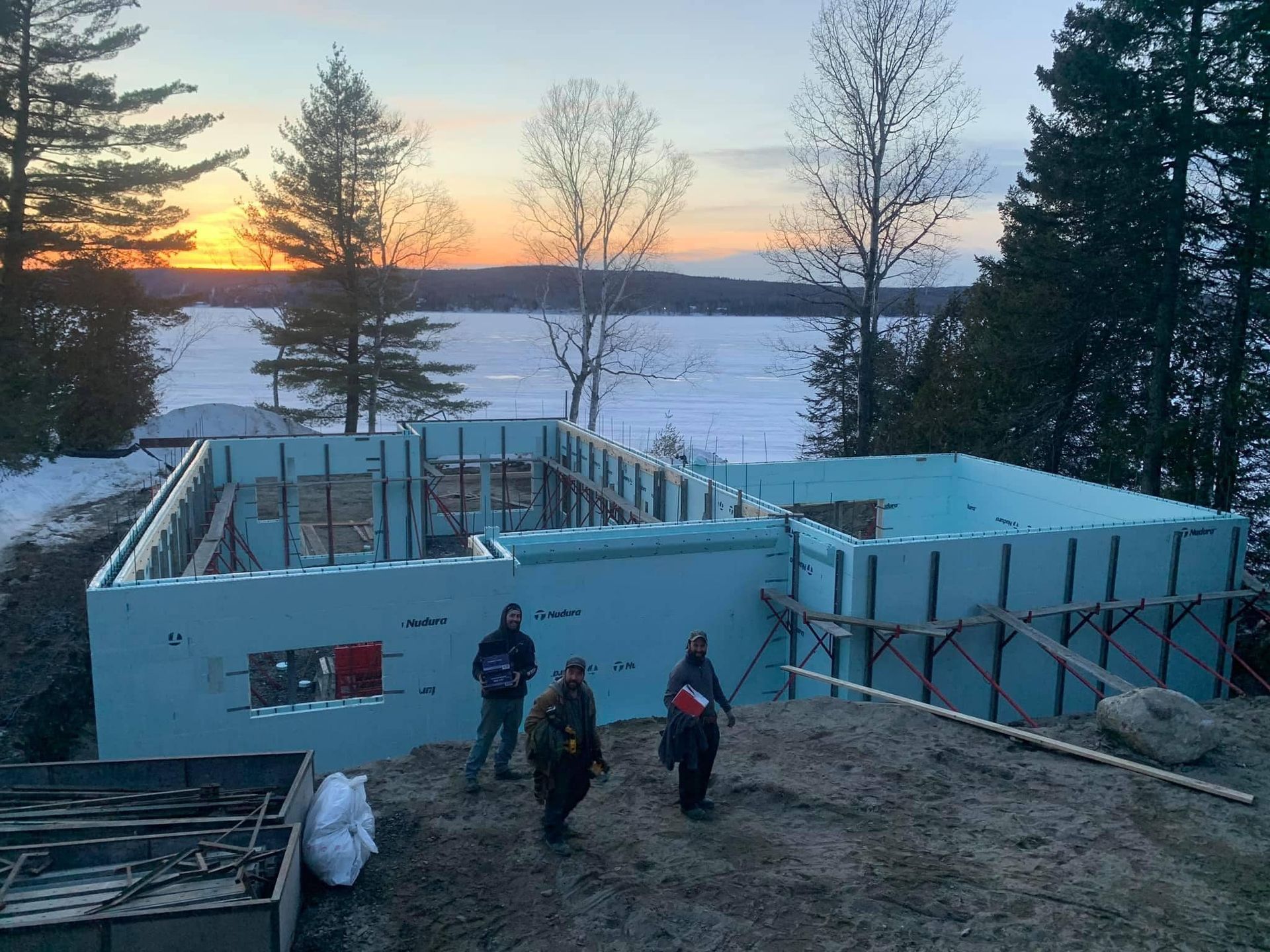 Construction d'une maison avec des coffrages isolants. Quatre ouvriers sur un paysage enneigé au coucher du soleil.