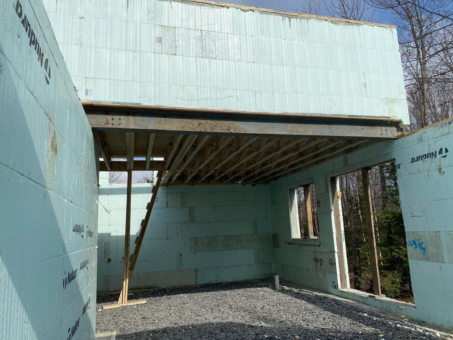 Intérieur d'une maison en construction avec murs en mousse bleue et poutres en bois pour un deuxième étage.