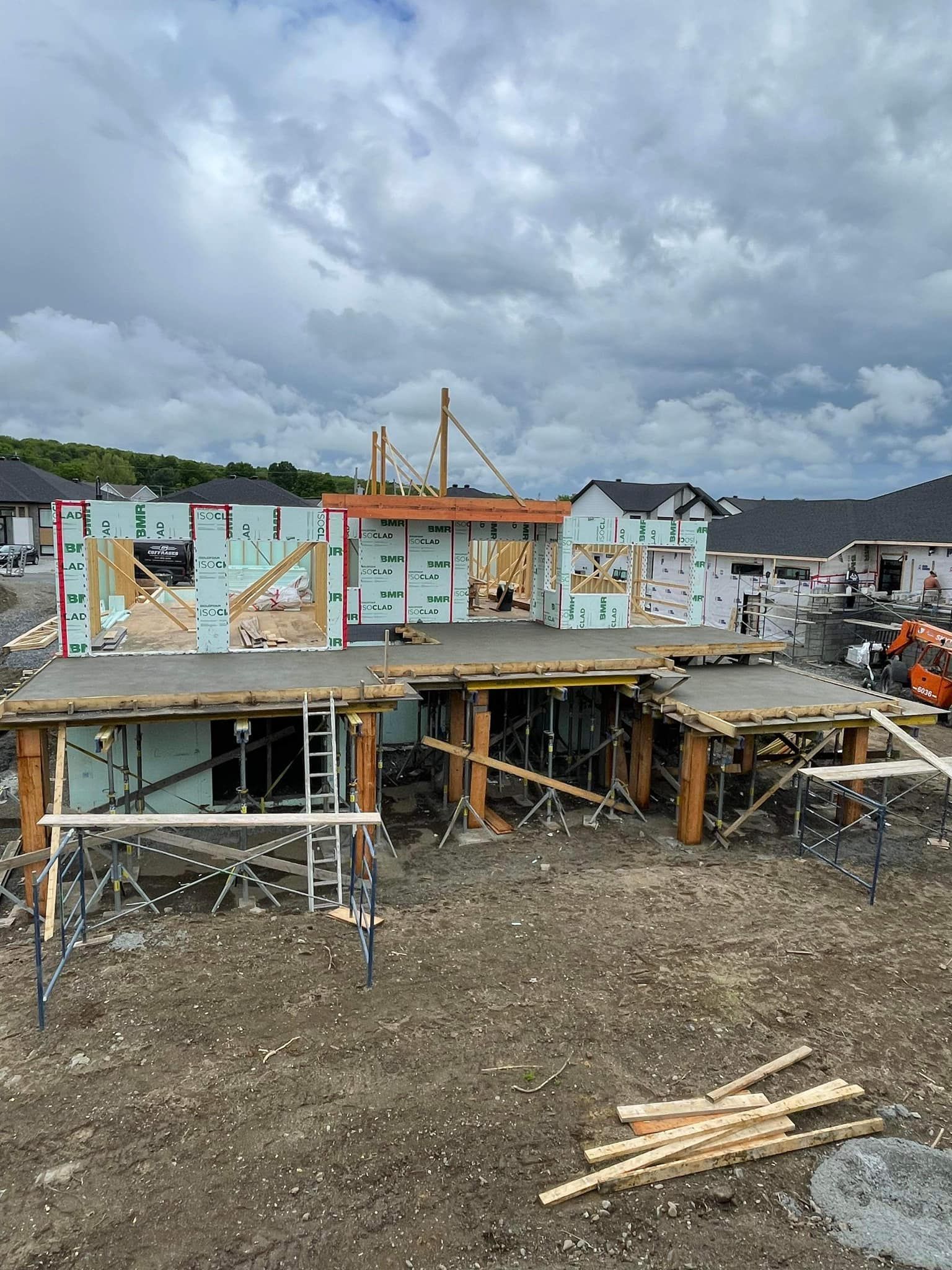 Chantier avec charpente et bétonnage en cours ; ciel nuageux.