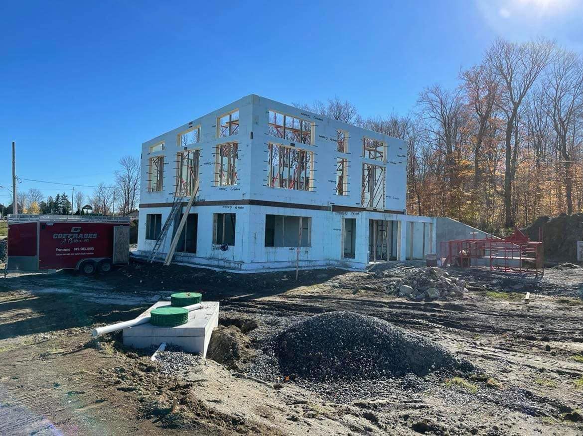 Bâtiment de deux étages en construction sur un terrain en terre avec murs blancs apparents.