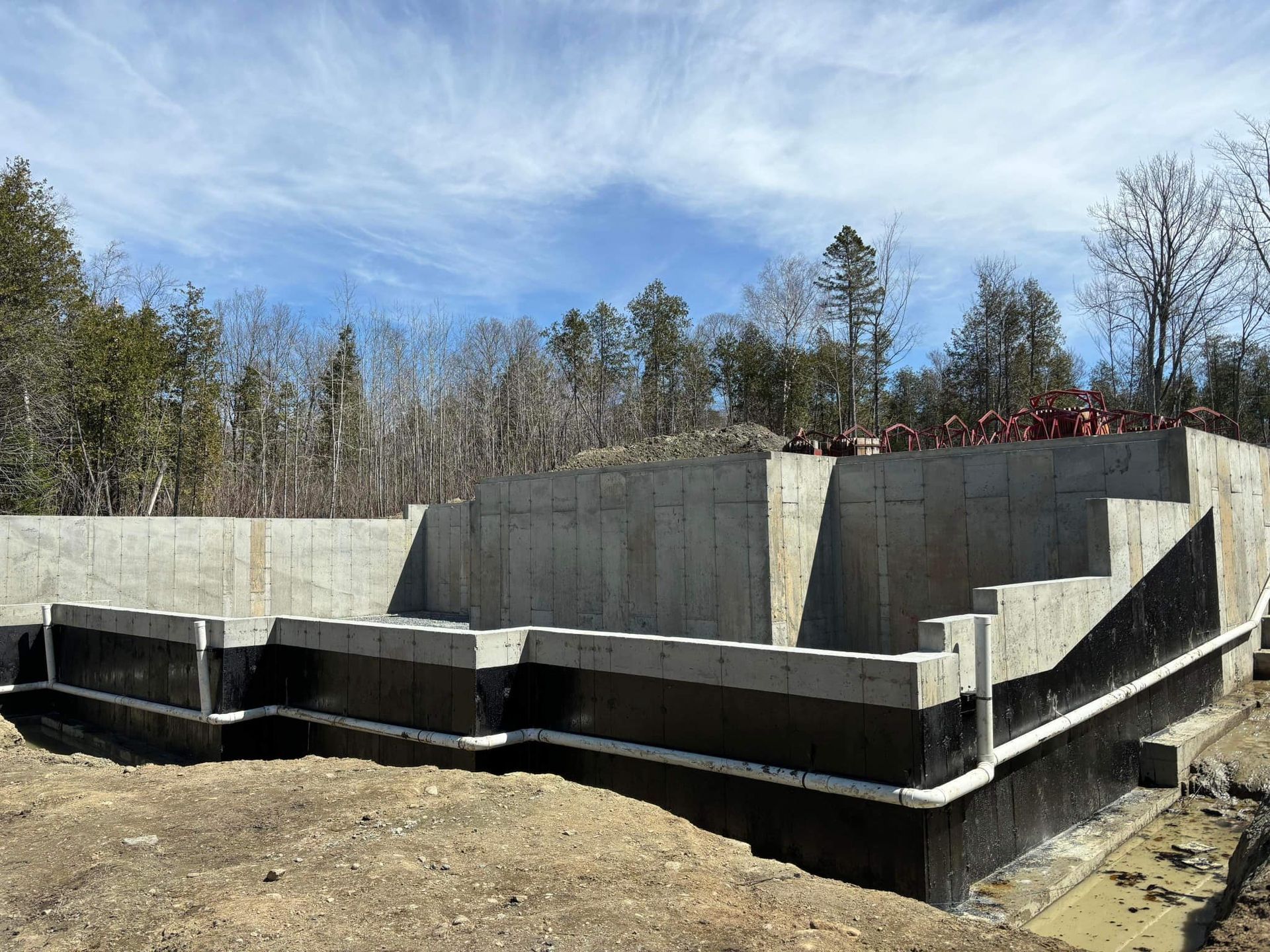 Murs de fondation en béton avec étanchéité noire et tuiles de drainage blanches.
