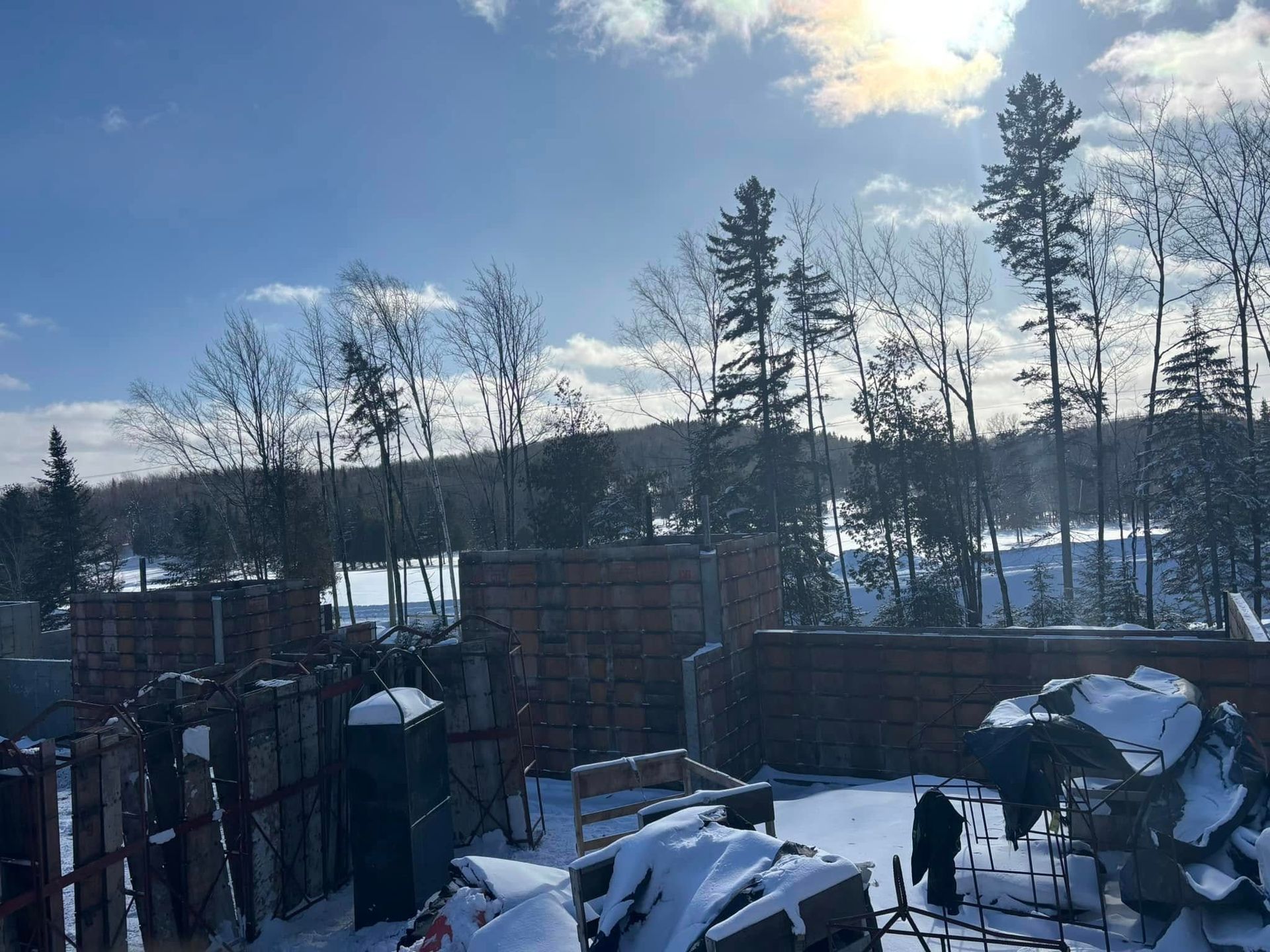 Paysage enneigé avec des arbres et un plan d'eau partiellement obscurci ; des piles de bois au premier plan.