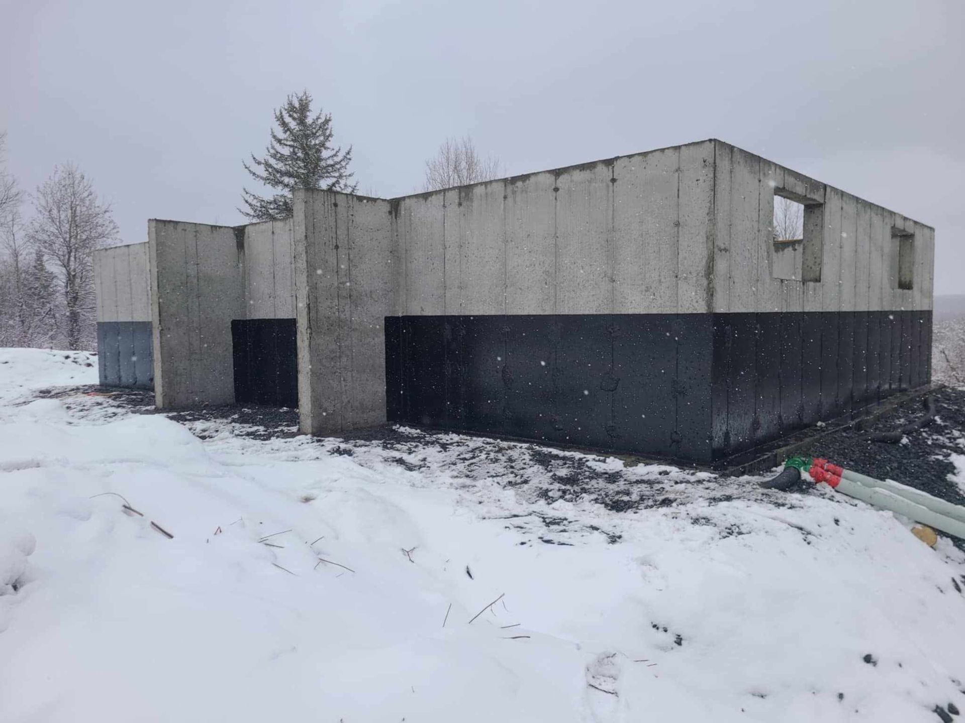 Fondation en béton d'un bâtiment en construction, recouverte d'isolant noir, dans un paysage enneigé.
