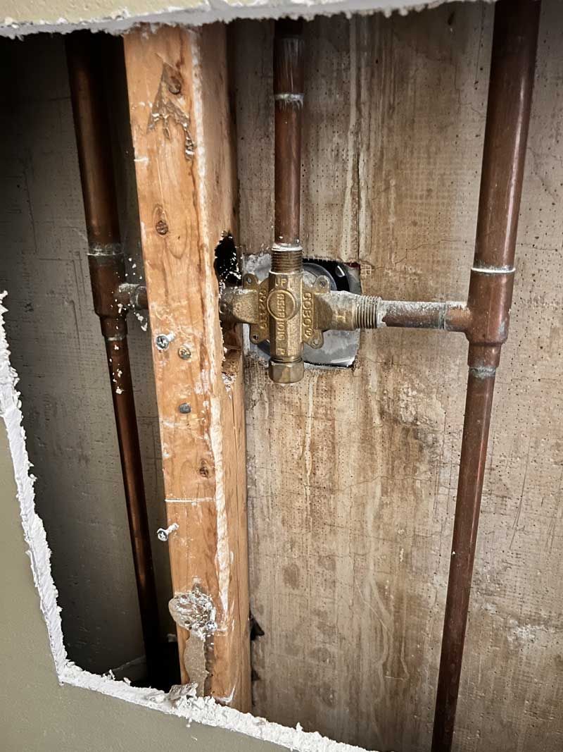 Copper pipes and a shower valve are exposed inside a wall.