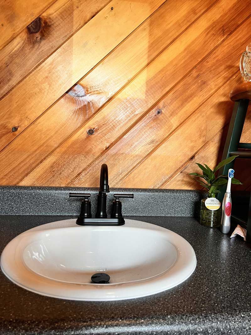 Bathroom sink with white basin, black faucet, and dark countertop against a wooden wall.