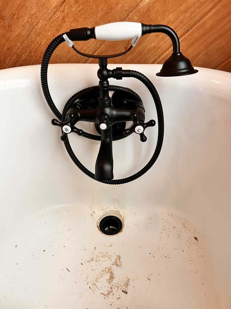 Black vintage bathtub faucet over a white tub with visible dirt and drain.