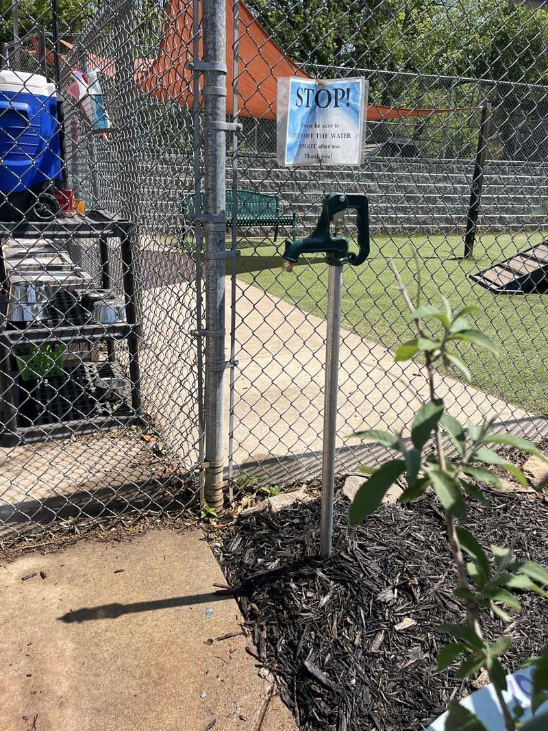 Chain link fence with gate, green handle, sign, and grassy area.