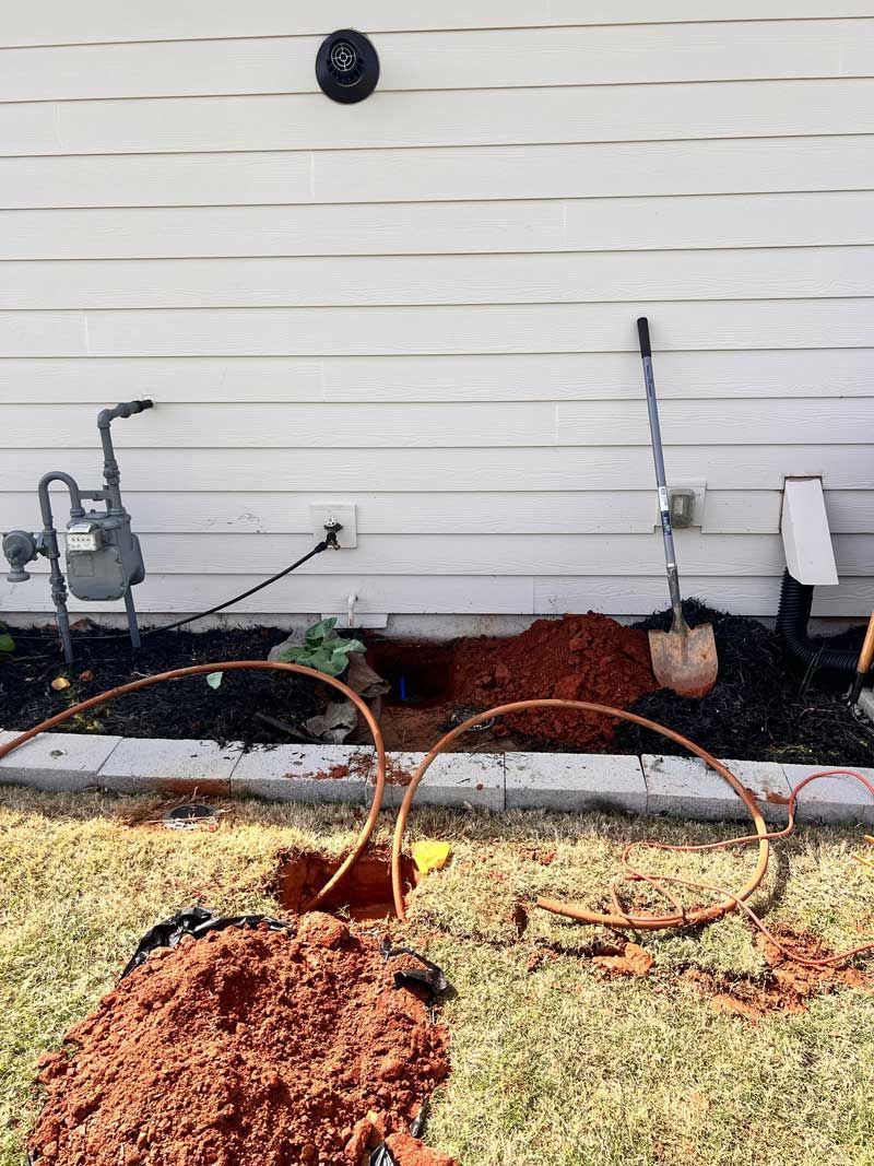 A yard with a hole dug near a house wall, gas meter, and exposed copper tubing.